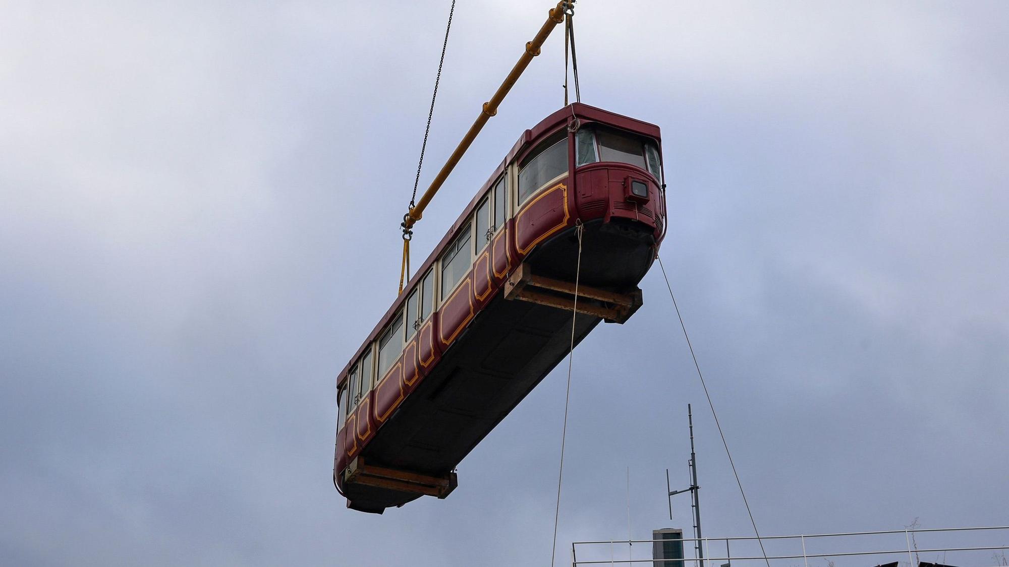 Ein großer Kran hat das Fahrzeug von einem Tieflader auf eine Stahlkonstruktion zwischen zwei Gebäuden gehoben.