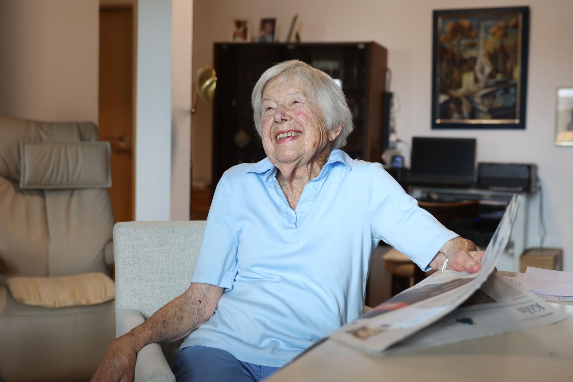 Helga Schmitt wieder am Tisch mit Zeitung, sie lacht.