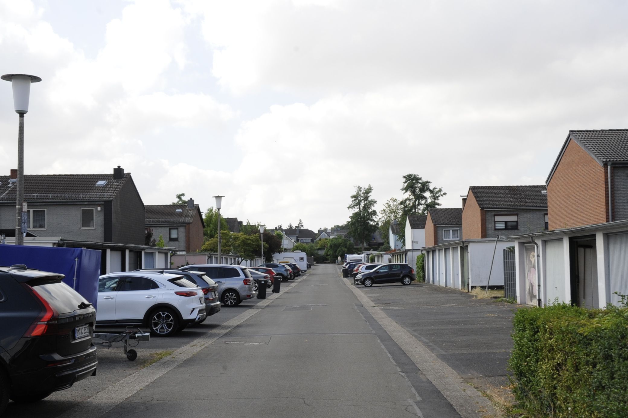 Zu sehen ist eine Straße mit Garagen und parkenden Autos davor, dahinter sind Häuser zu sehen.
