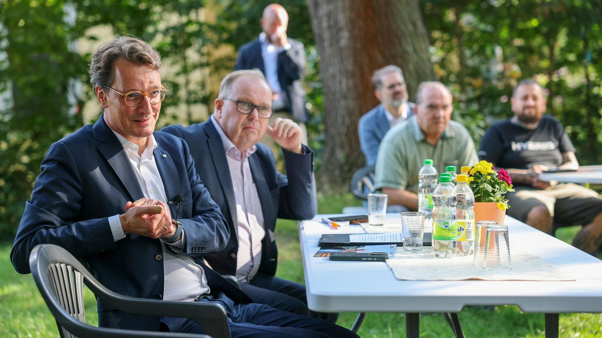 Hendrik Wüst (l, CDU), Ministerpräsident von Nordrhein-Westfalen, und Michael Scheffler (CDU), Landtagsabgeordneter Sachsen-Anhalt, sitzen im Garten eines Dorfgemeinschaftshauses und sprechen mit Bürgern.