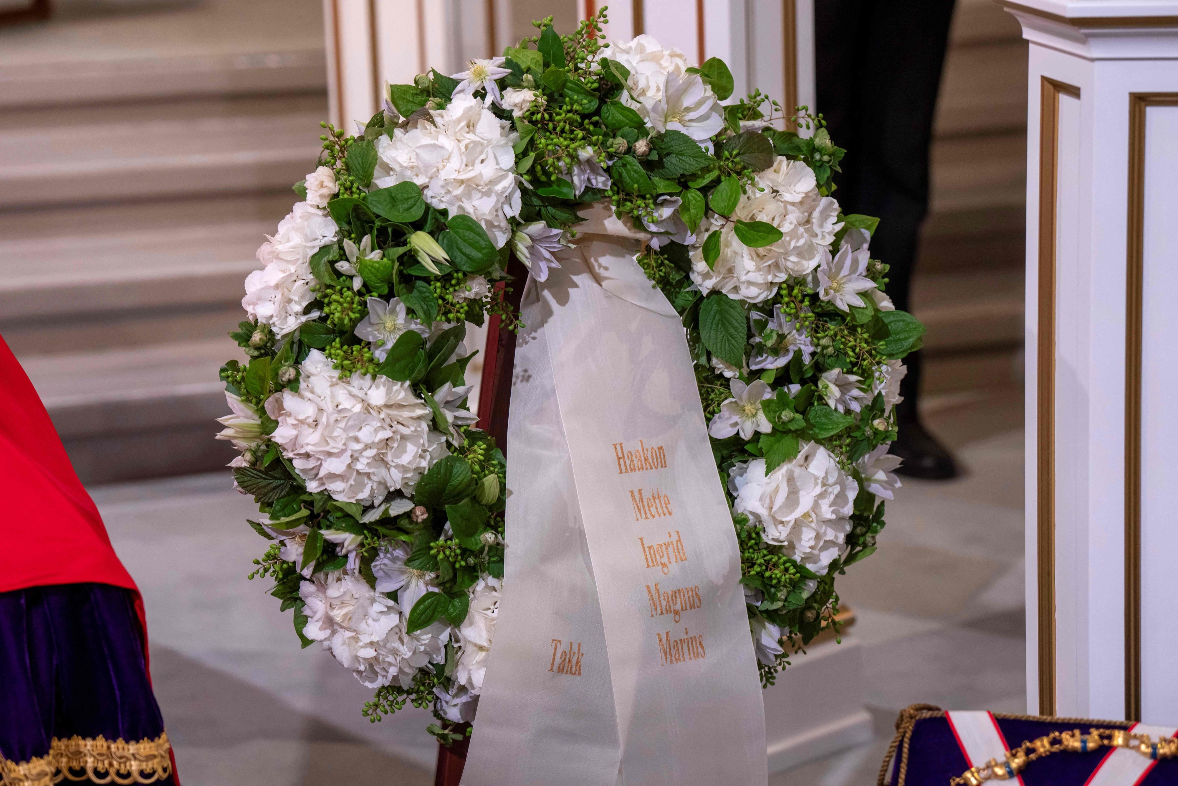 Explizite Nennung auf der Trauerschleife: Marius Borg Høiby wird namentlich zusammen mit dem neuen König Haakon VIII., Königin Mette-Marit, Kronprinzessin Ingrid Alexandra und Prinz Sverre Magnus auf dem Kranzband mit der Aufschrift „Danke“ („Takk“) aufgeführt.