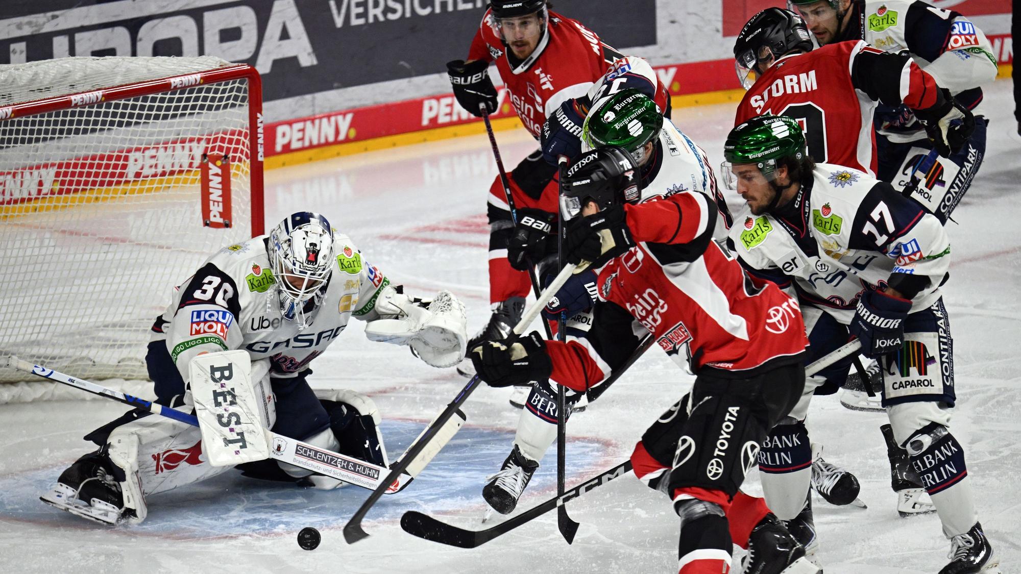 Dominik Bokk (Kölner Haie) und Torwart Jake Hildebrand (Eisbären Berlin) kämpfen auf dem Eis um den Puck.