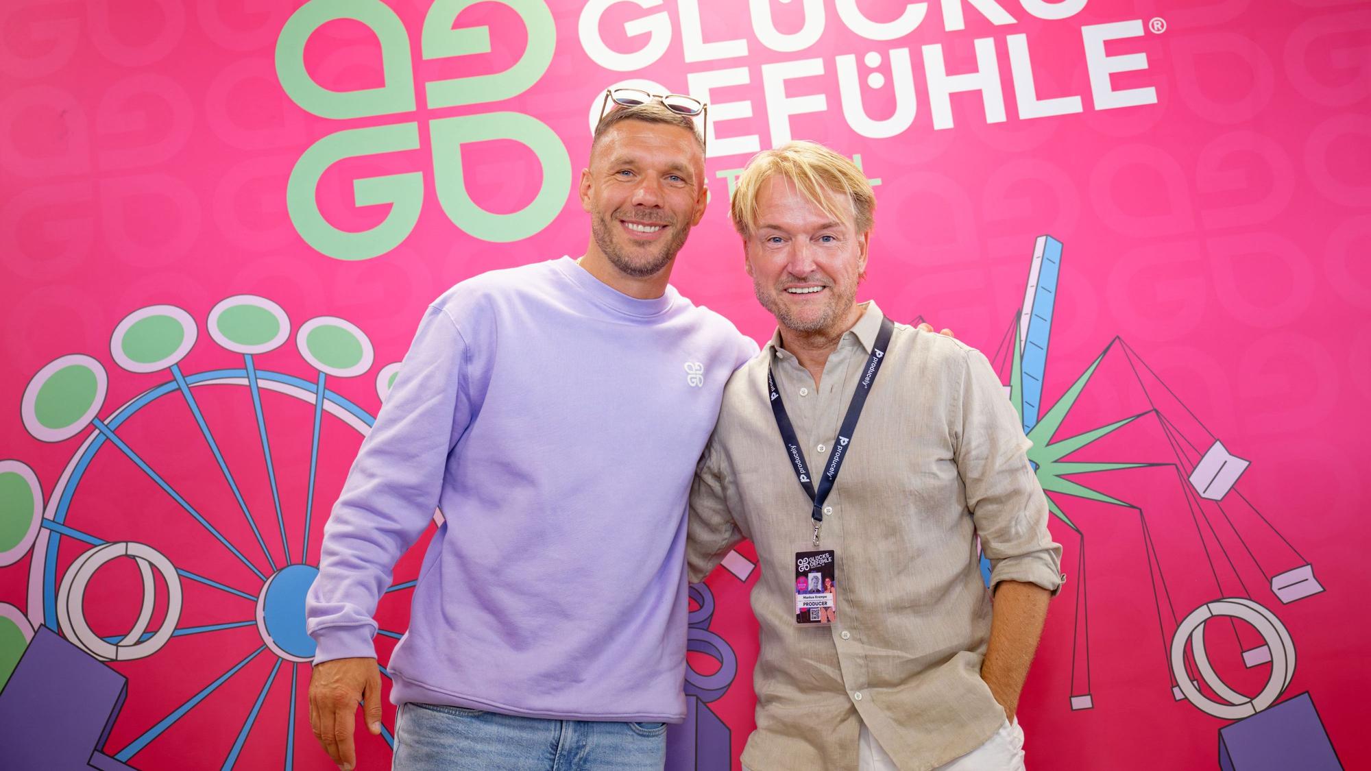 Der Fußballspieler Lukas Podolski (l.) und Musikmanager Markus Krampe stehen auf dem Hockenheimring während einer Pressekonferenz vor einem Logo des Glücksgefühle-Festivals. (Archivbild)
