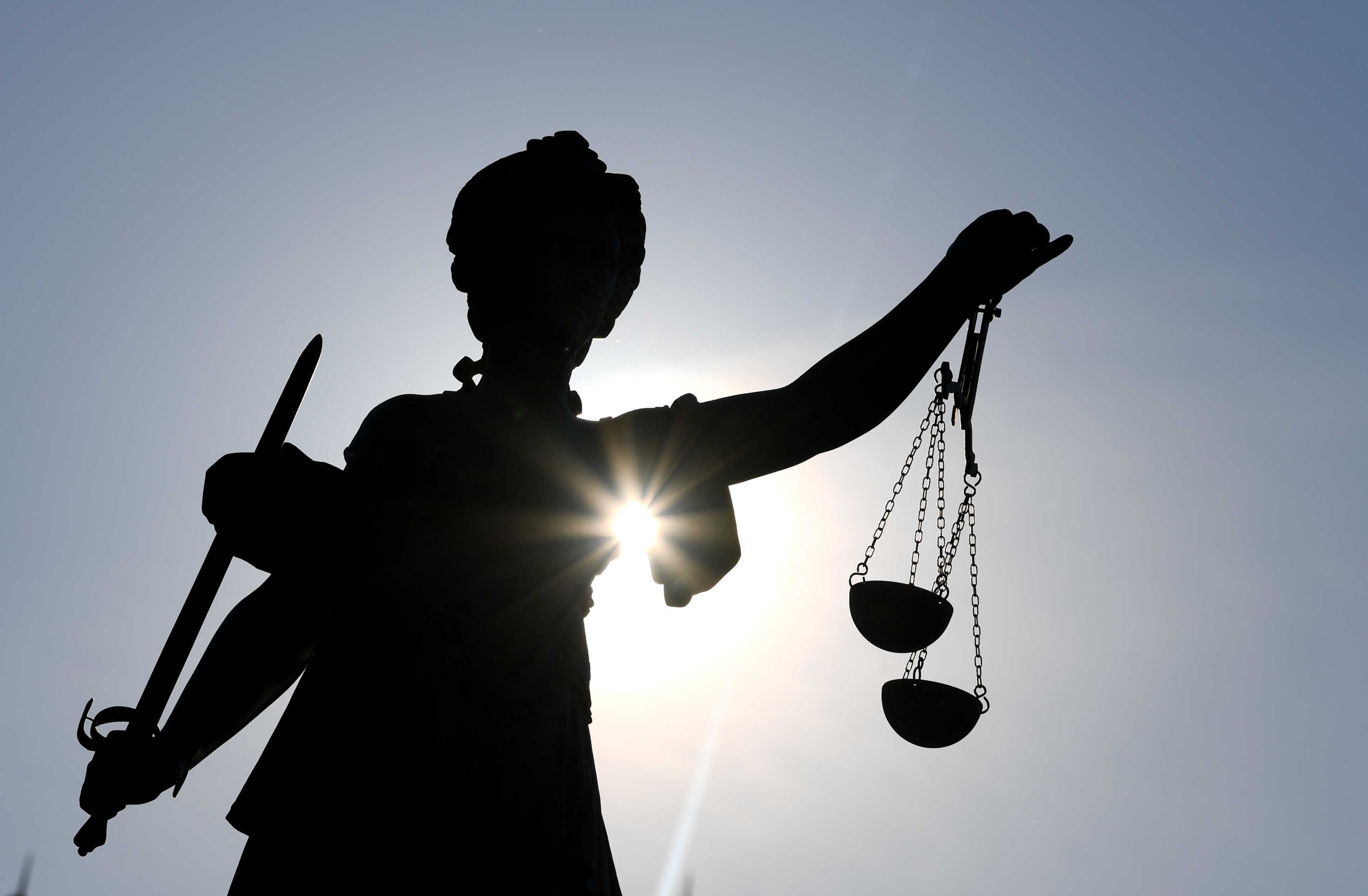 Eine Bronze der Justitia hält zwei Waagschalen ins Gegenlicht.