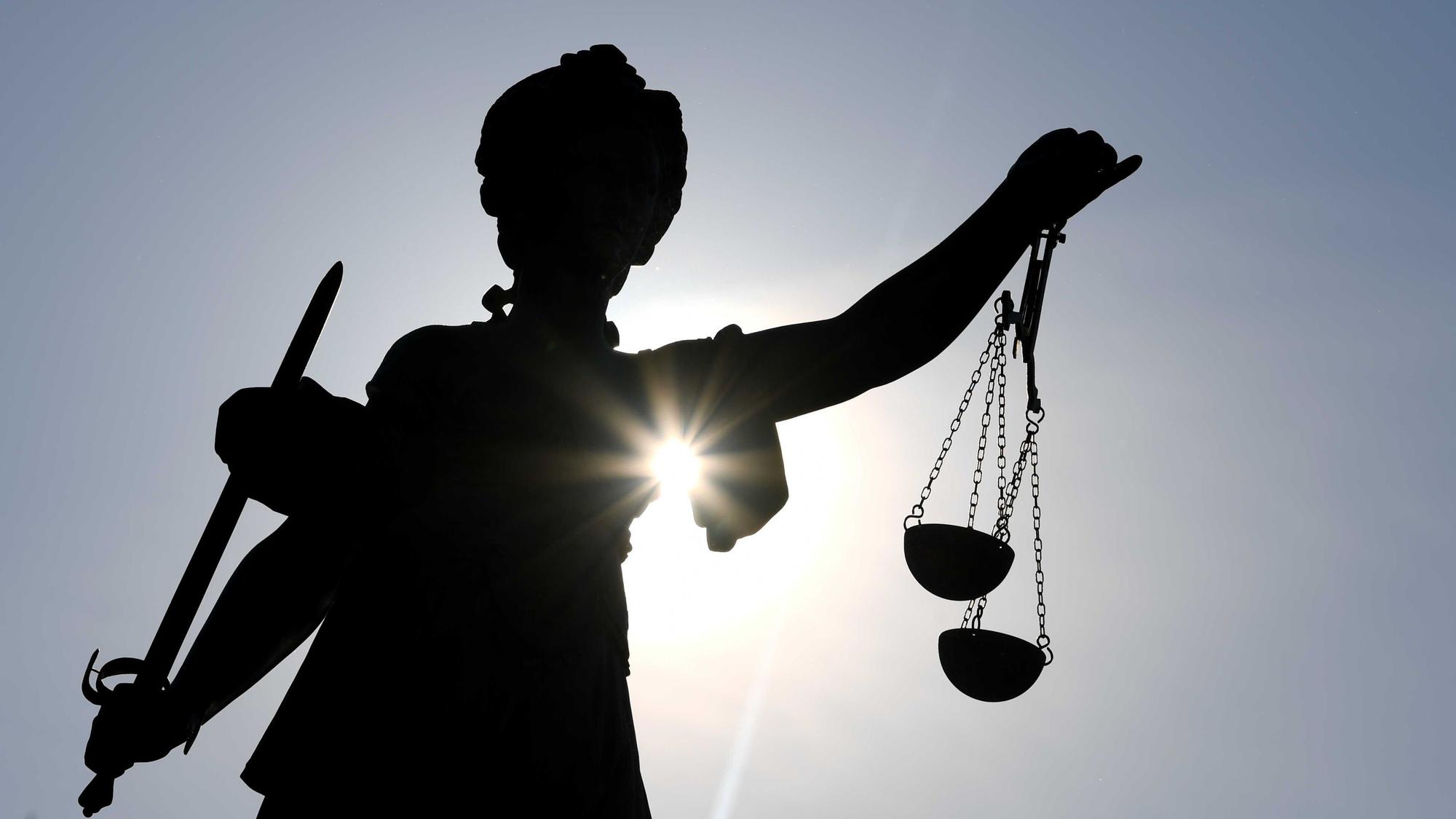 Eine Bronze der Justitia hält zwei Waagschalen ins Gegenlicht.