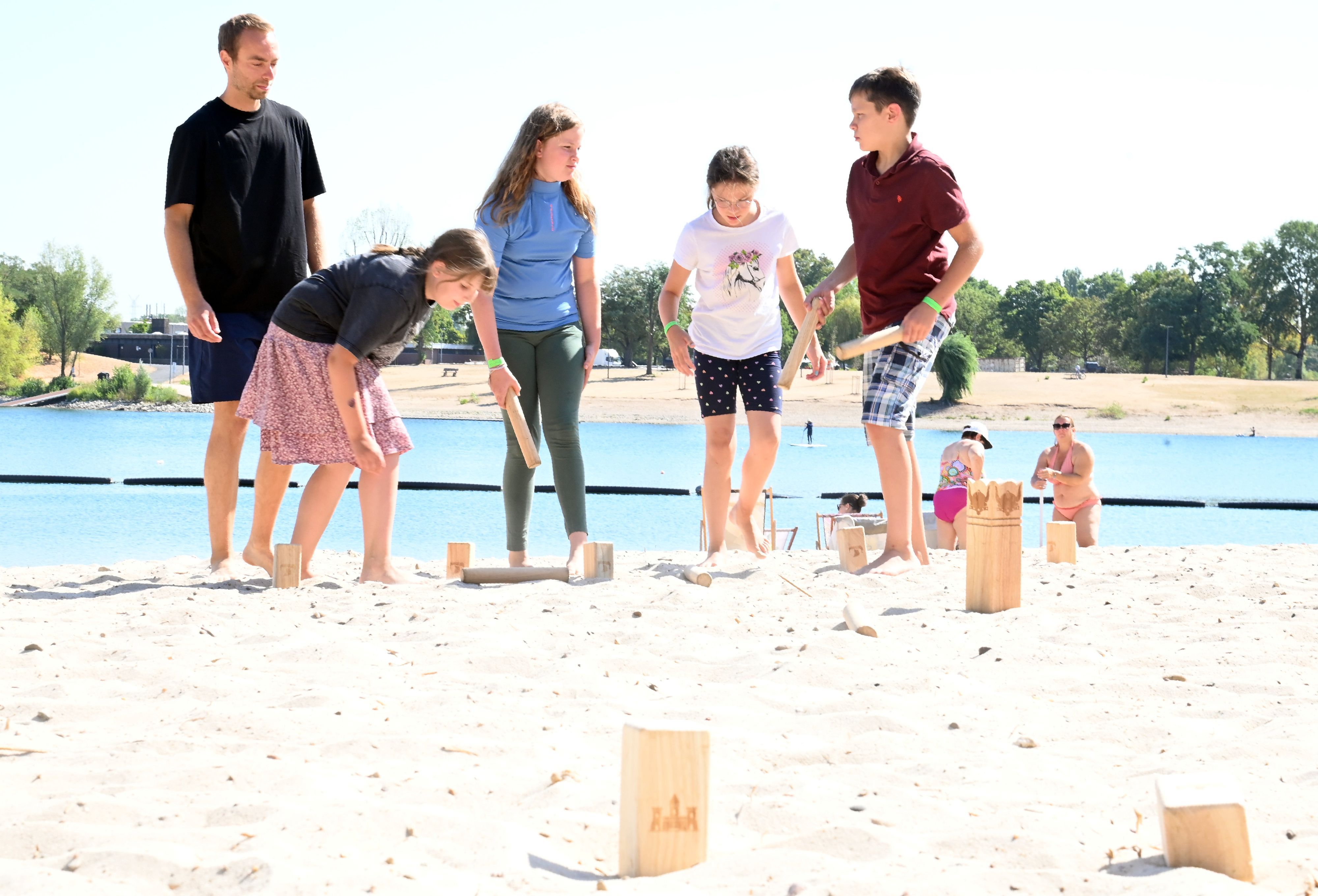 Ein Mitarbeiter des Vereins Bunter Kreis Rheinland e.V. steht mit vier Geschwistern von schwerkranken Kindern am Strand des Fühlinger Sees und spielt mit ihnen Wikingerschach.