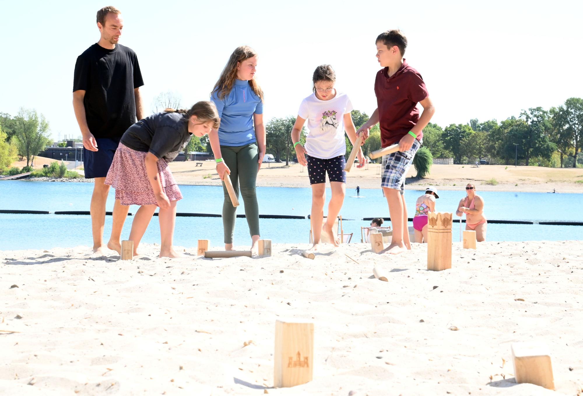Ein Mitarbeiter des Vereins Bunter Kreis Rheinland e.V. steht mit vier Geschwistern von schwerkranken Kindern am Strand des Fühlinger Sees und spielt mit ihnen Wikingerschach.