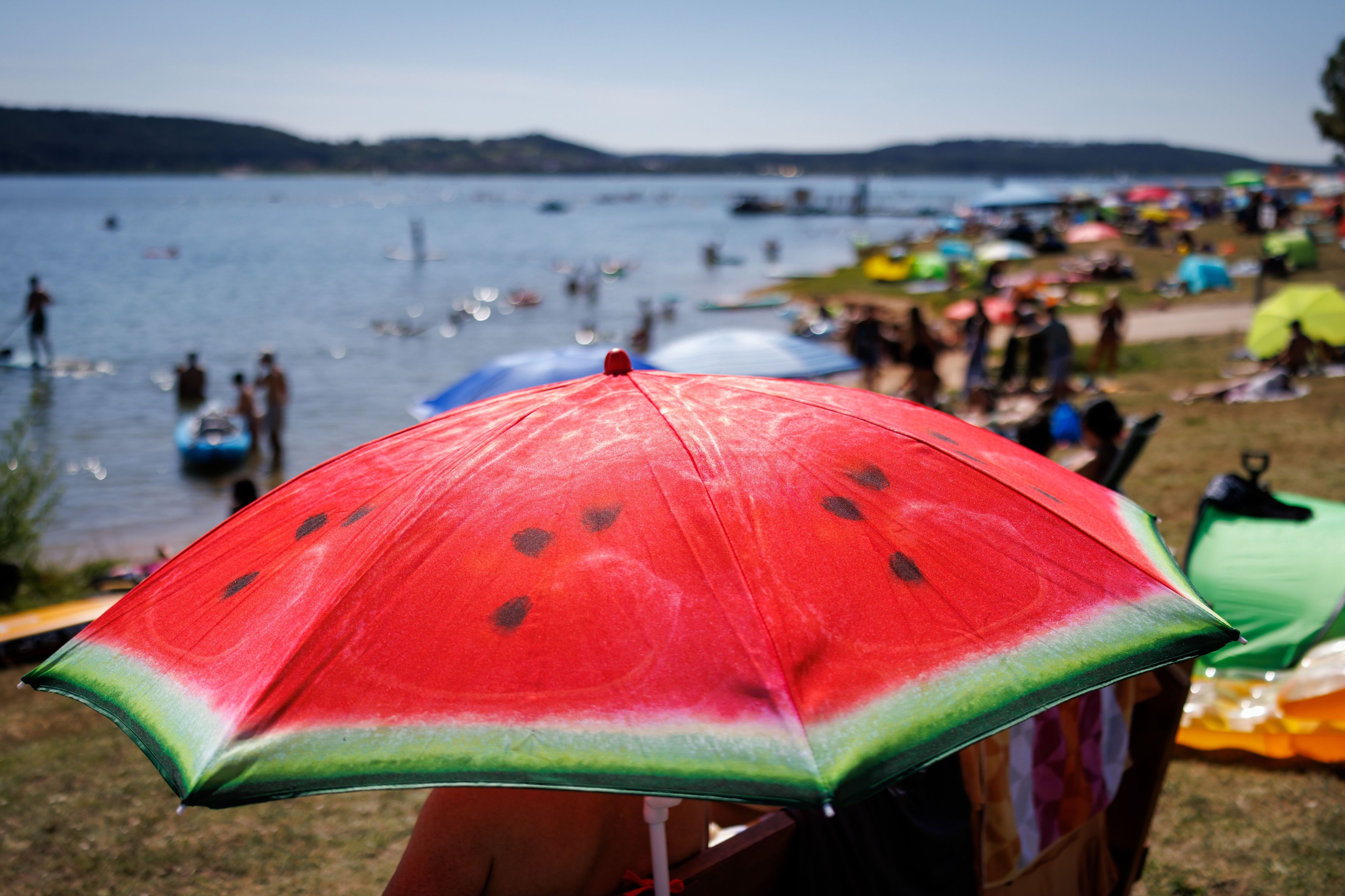 Ein Sonnenschirm mit dem Aufdruck einer Wassermelone steht am Sonntag bei heißem Wetter am gut besuchten Badestrand am Brombachsee.