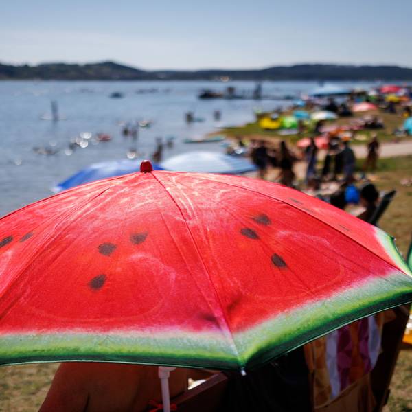 Ein Sonnenschirm mit dem Aufdruck einer Wassermelone steht am Sonntag bei heißem Wetter am gut besuchten Badestrand am Brombachsee.