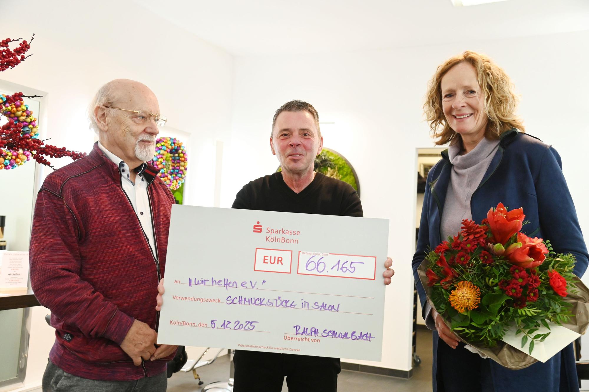 Der Goldschmiedemeister Herbert Schmelzer und Friseurmeister Ralph Schwalbach überreichen Isabella Neven DuMont von wir helfen e.V. einen symbolischen Scheck in Höhe von 66.165 Euro