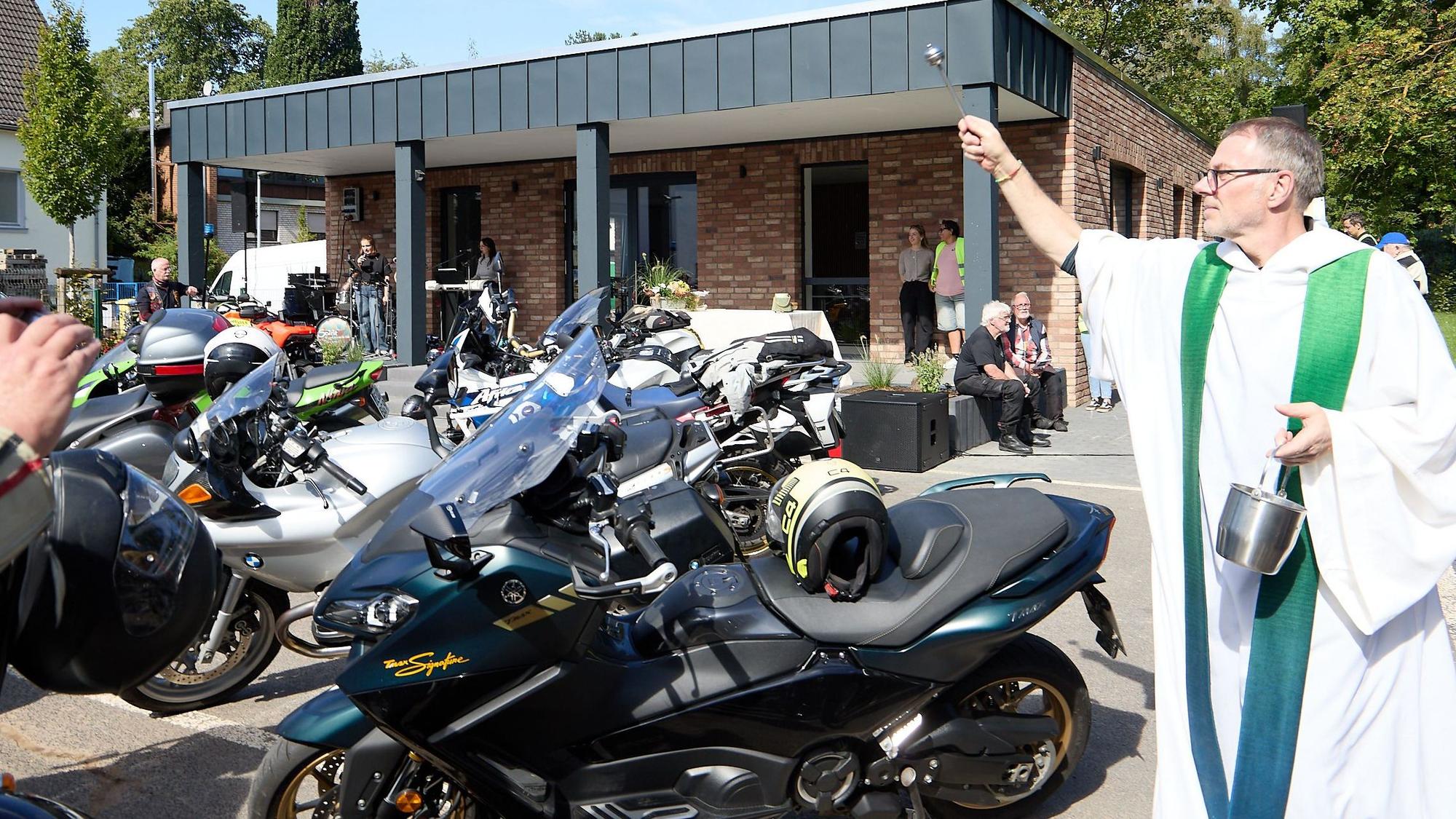 Pfarrer Hardy Hawinkels trägt ein Priestergewand und segnet Motorräder.