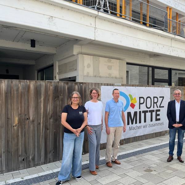 Fünf Personen stehen vor einem Bauzaun vor einem Rohbau.