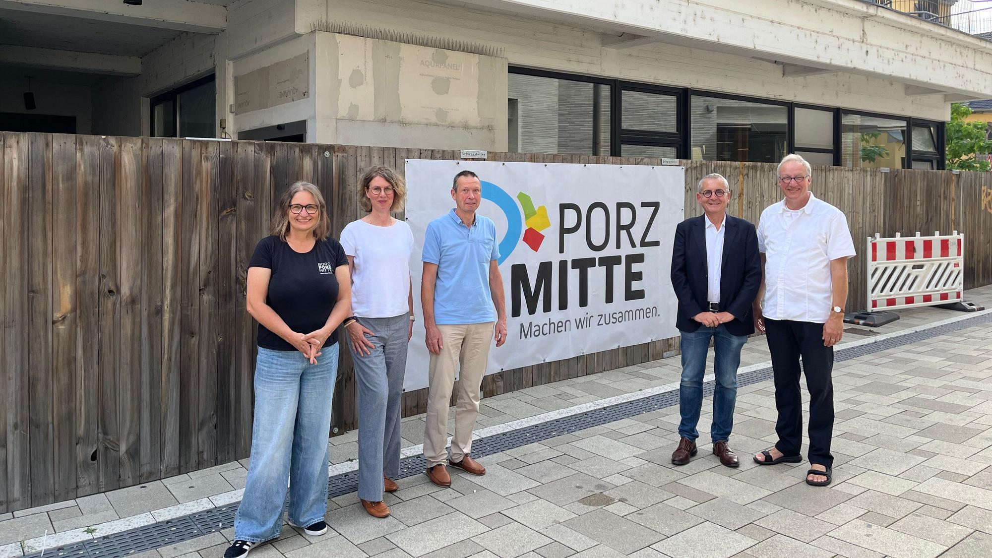 Fünf Personen stehen vor einem Bauzaun vor einem Rohbau.