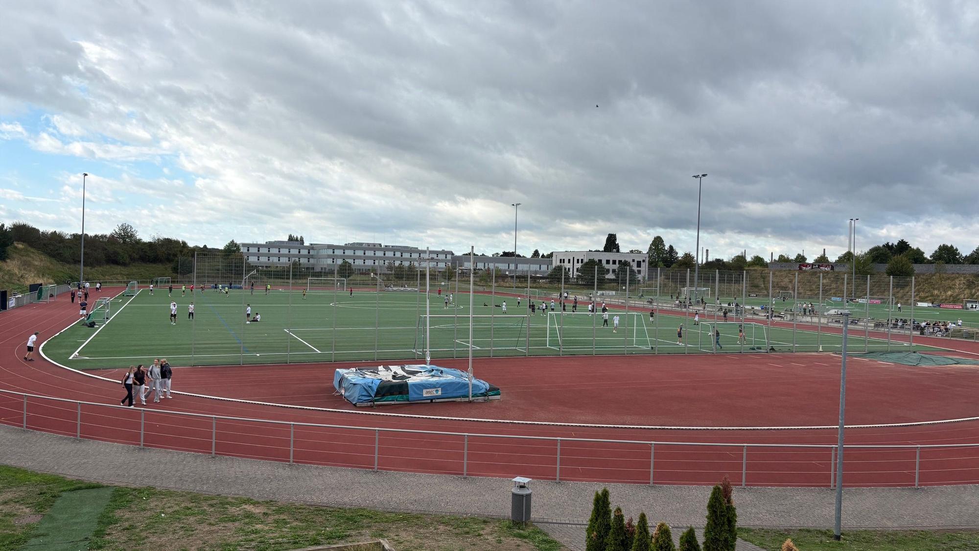 Eine Sportanlage mit großem Kunstrasenfeld und einer roten Tartanbahn drumherum.