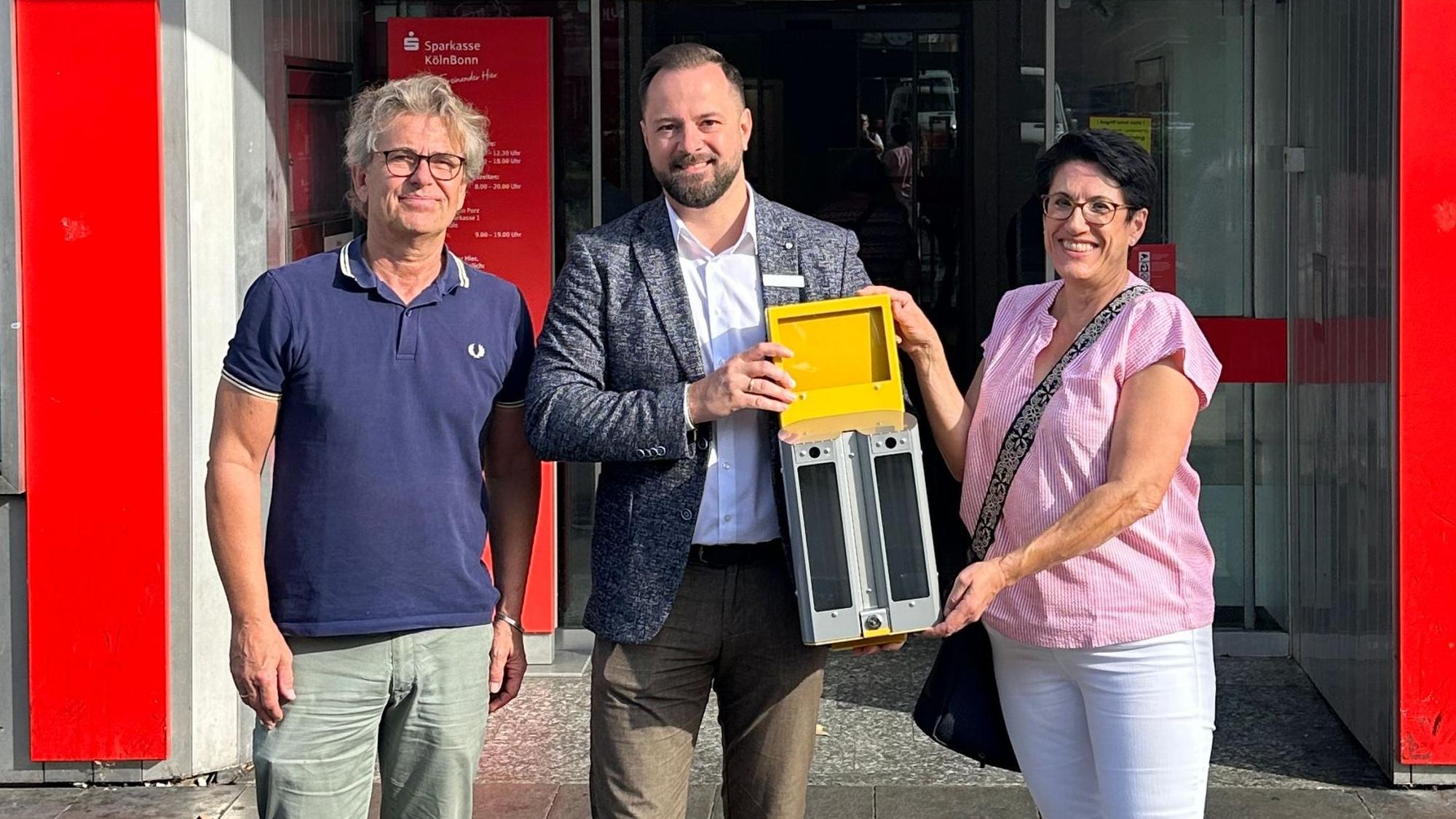 Zwei Männer und eine Frau stehen vor einer Sparkassen-Filiale.