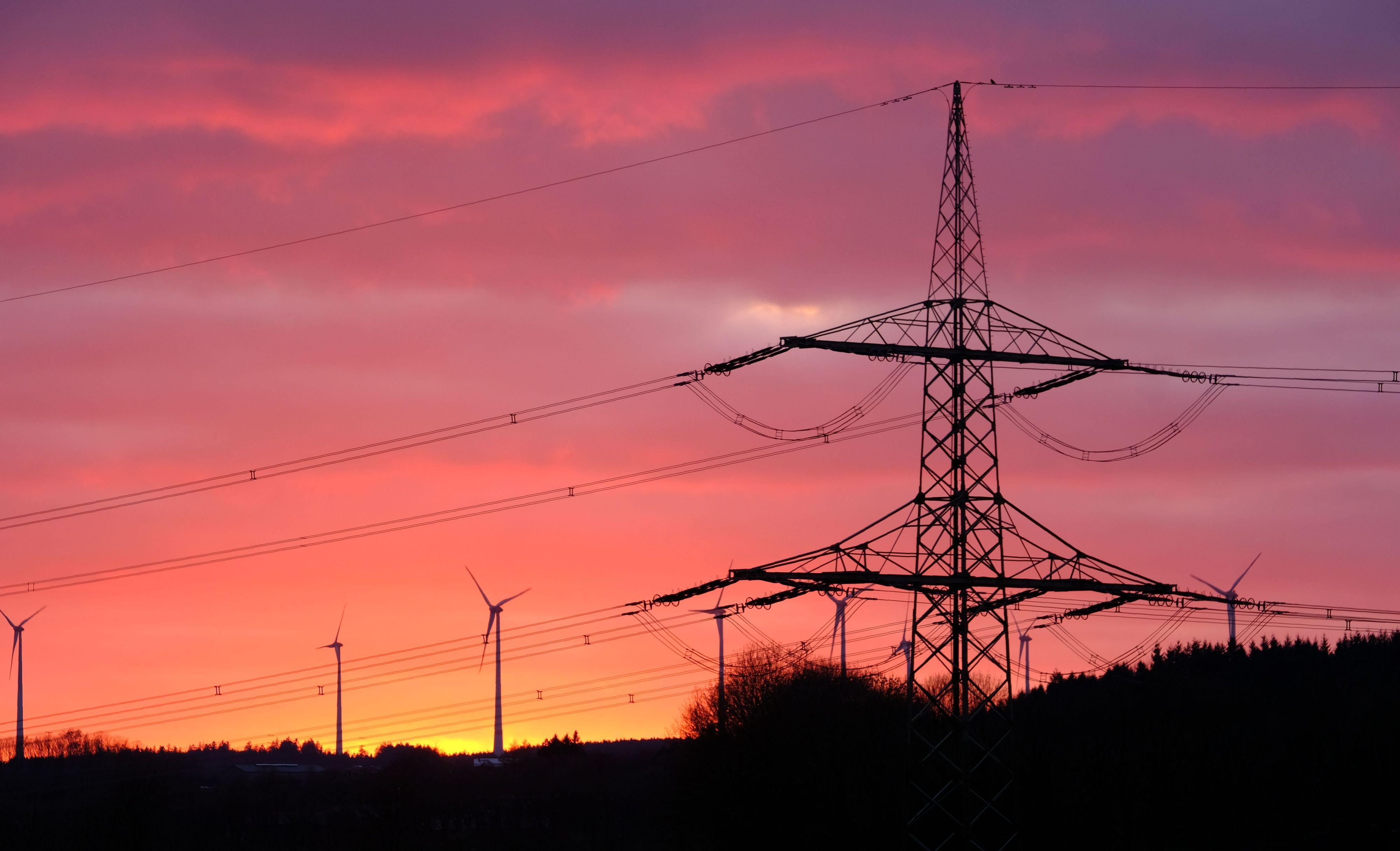 Der Mast ener 110-kV-Höchstspannungsleitung und mehrere Windkraftanlagen im Abendrot bei Dahlem-Schmidtheim.