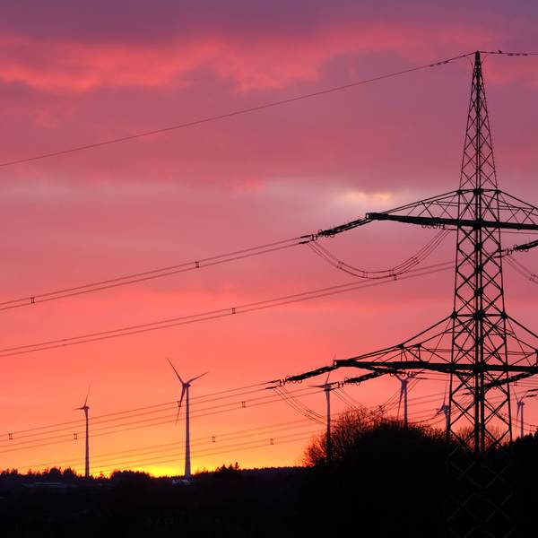 Der Mast ener 110-kV-Höchstspannungsleitung und mehrere Windkraftanlagen im Abendrot bei Dahlem-Schmidtheim.