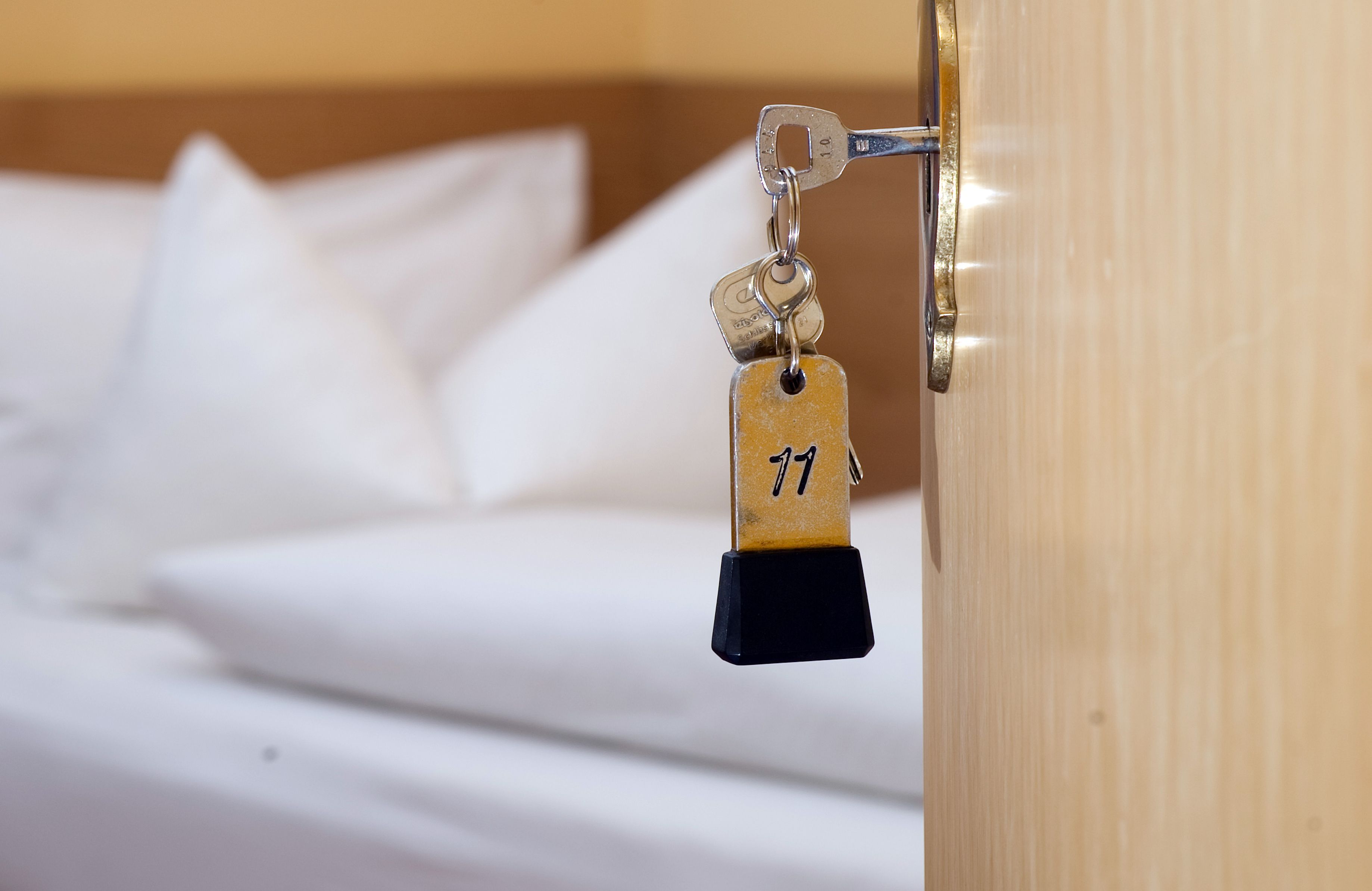 Ein Zimmerschlüssel hängt vor einem Bett im Türschloss.
