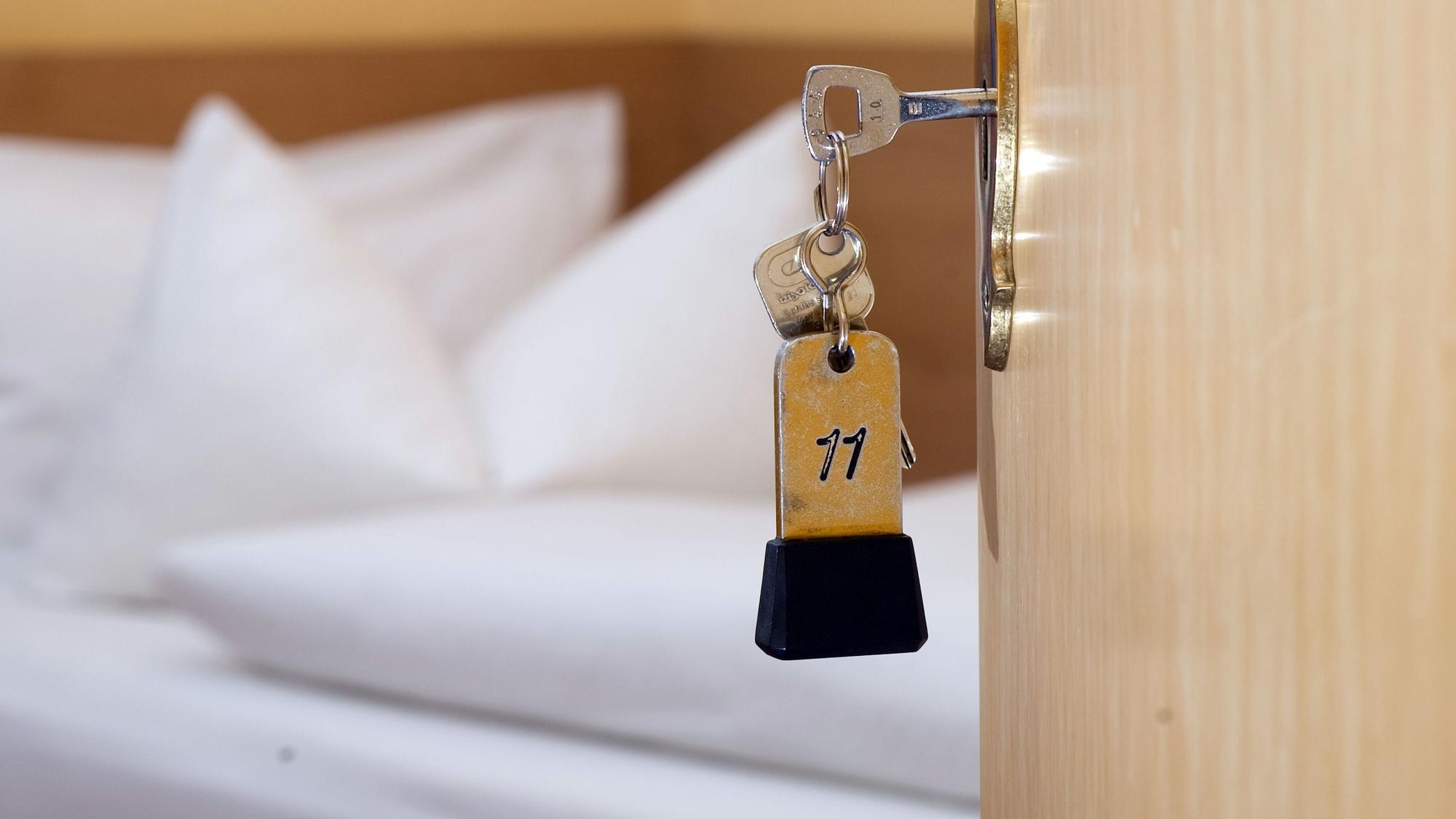 Ein Zimmerschlüssel hängt vor einem Bett im Türschloss.