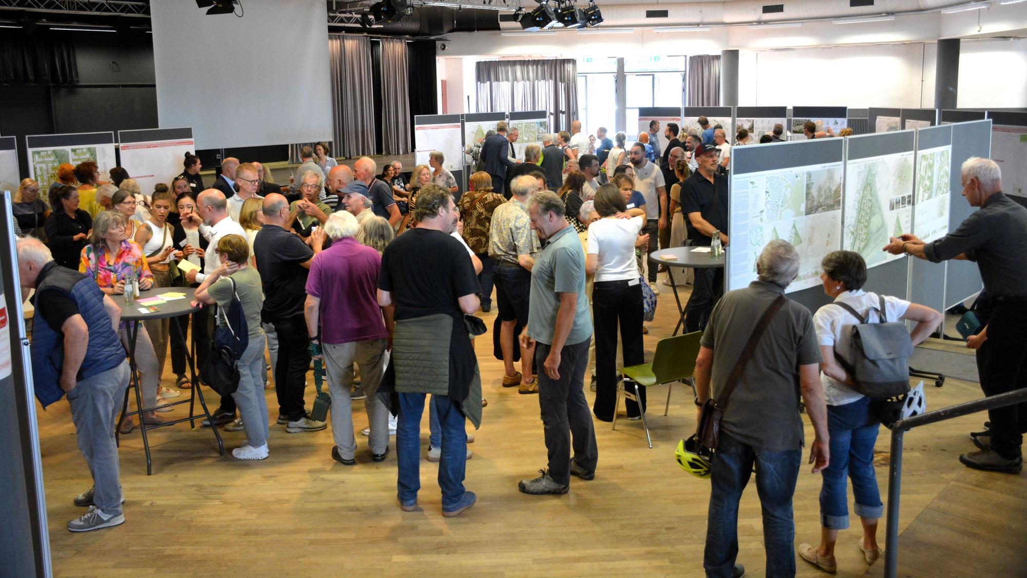 Viele Menschen stehen vor Infotafeln und sprechen miteinander.