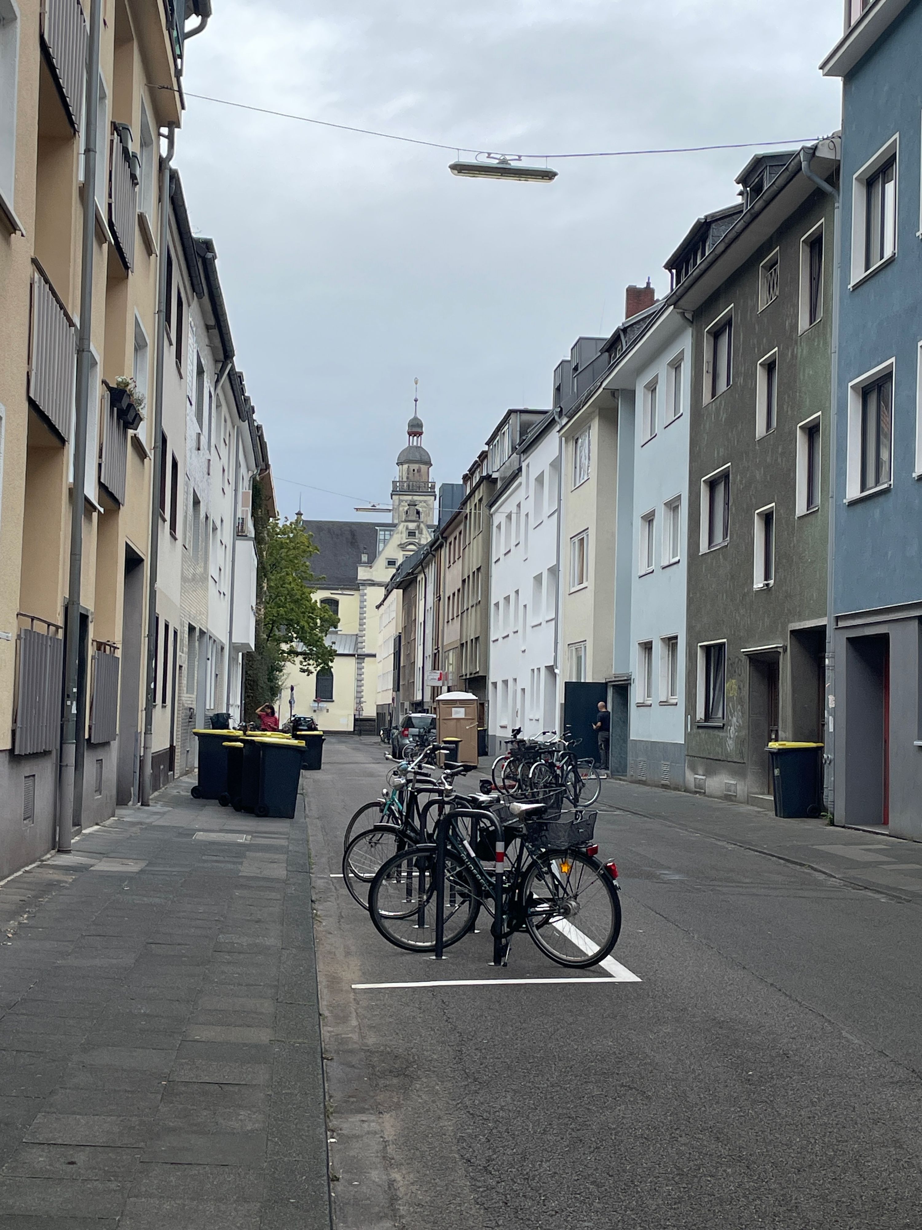 An einer schmalen, baumlosen Straße parken einige Fahrräder auf einer eingezeichneten Fläche.