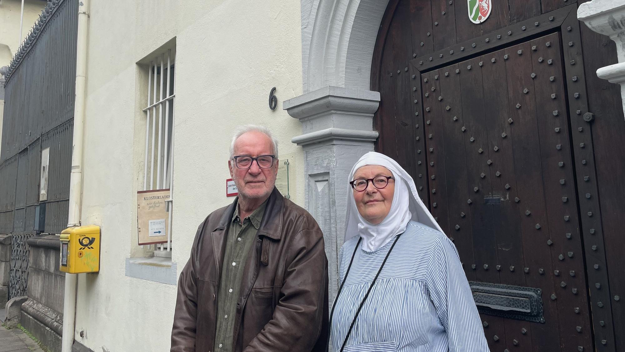 Ein Mann und eine Ordensschwester stehen vor einer schweren barocken Holztür.