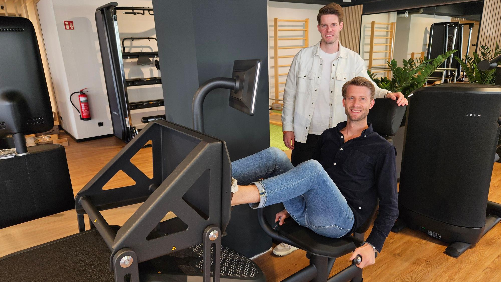 Henning Förster sitzt in einem Fitnessgerät, Steffen Förster steht dahinter.