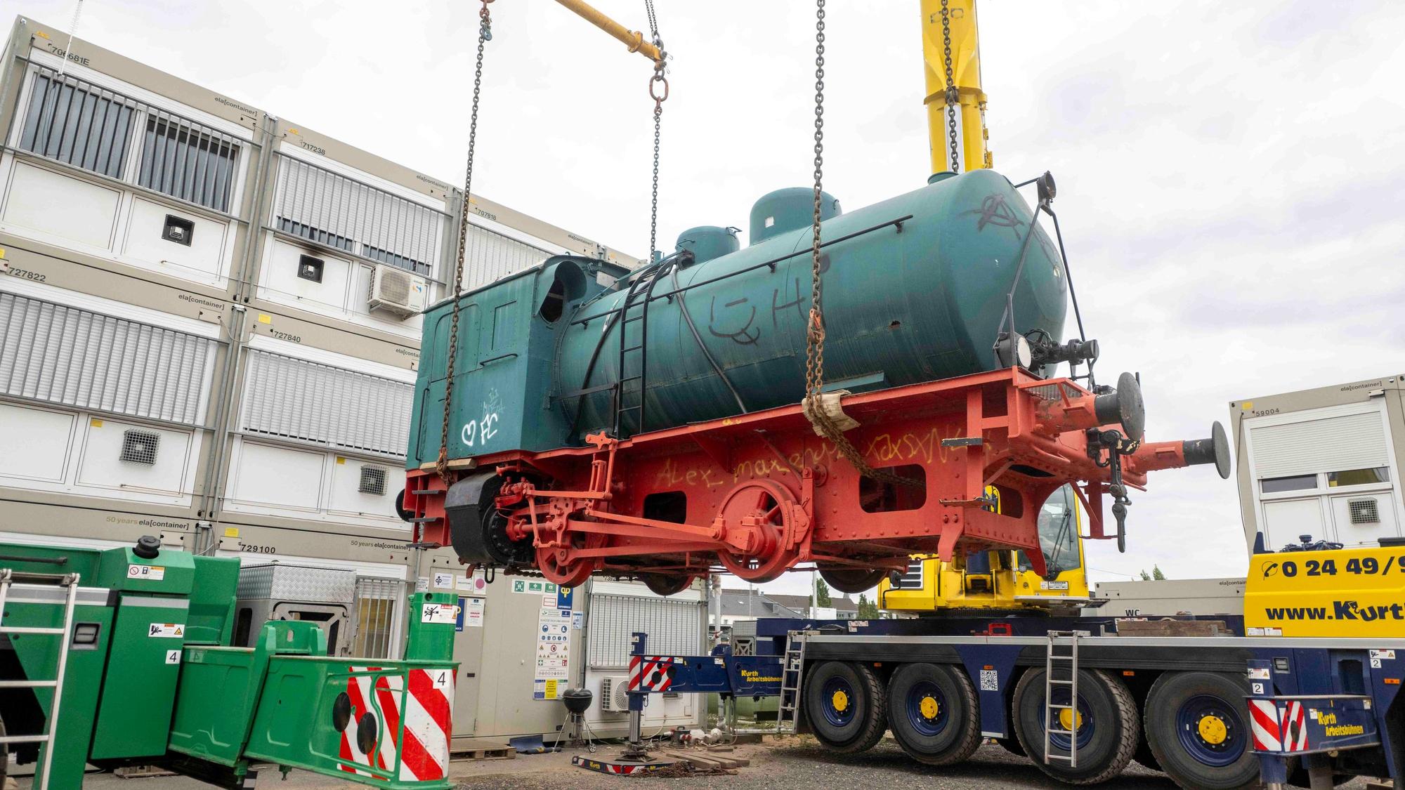 Die alte Lokomotive wird mit zwei Kränen auf einen Tieflader gehoben.