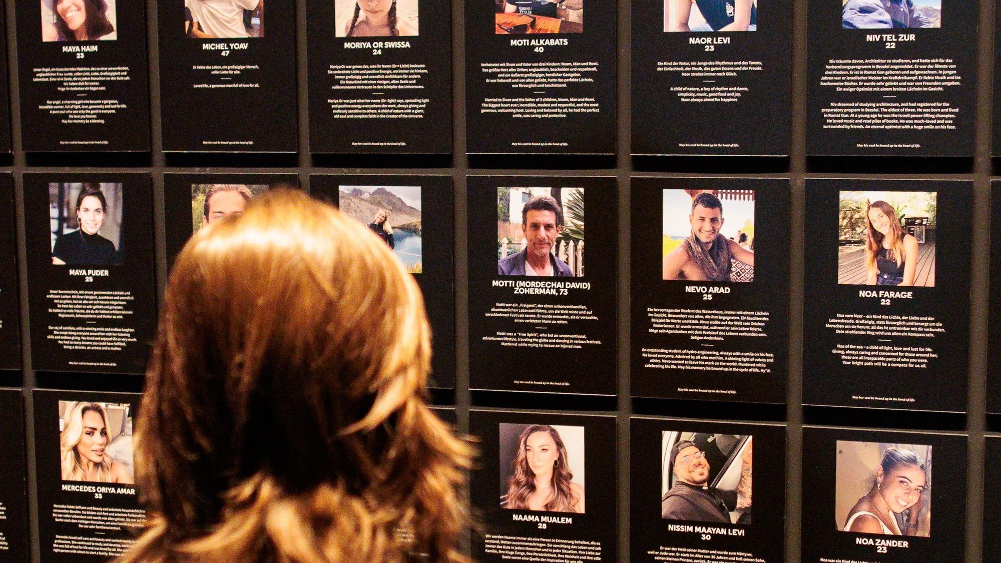Eine Besucherin steht bei einer Ausstellung vor einer Wand mit Bildern von Opfern des Terrorangriffs bei dem Musikfestival in Israel. Zu sehen sind zahlreiche Exponate vom Festivalgelände. (Archivbild)