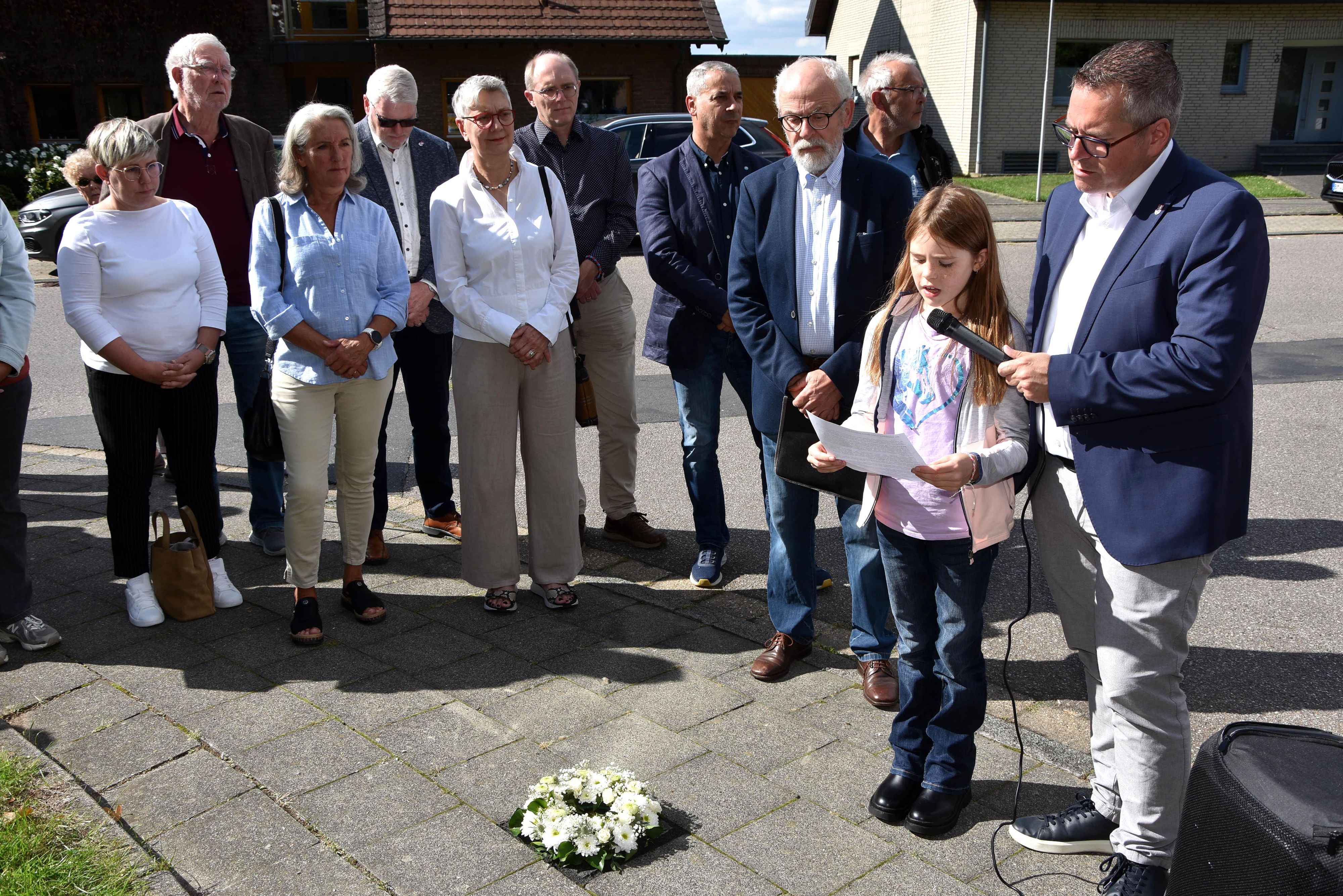 Zu sehen ist eine von Menschen umgebene Schülerin, die bei einer Stolperstein-Verlegung einen Text vorträgt.