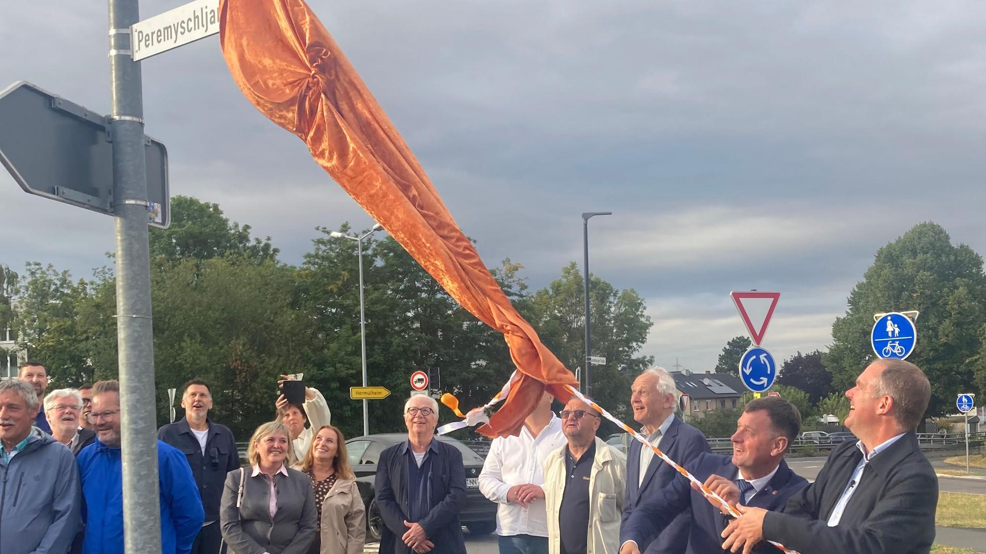 Das Foto zeigt eine Gruppe von Menschen bei der Enthüllung eines Straßenschilds.