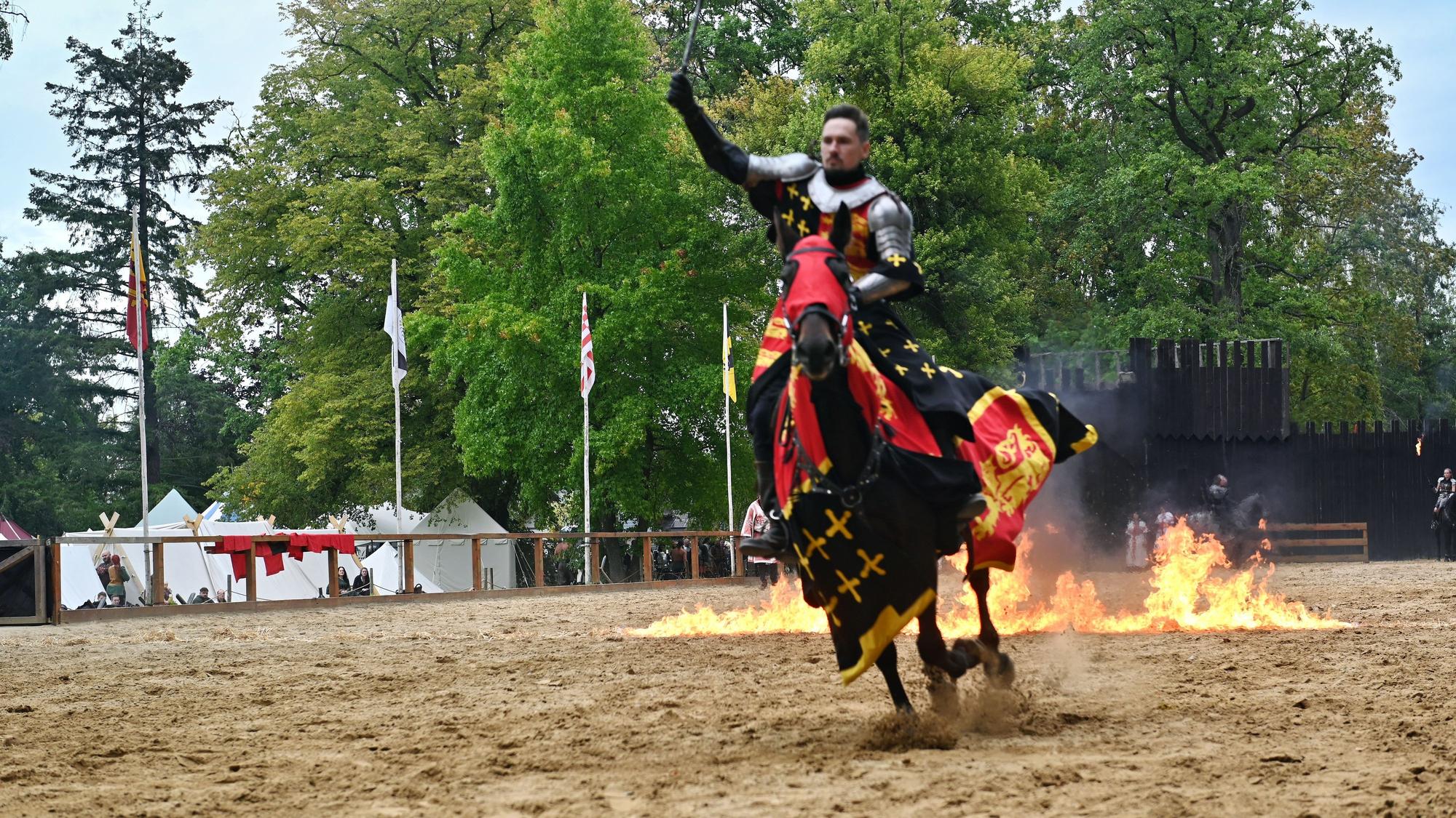 Ein Mann in Ritterrüstung reitet mit einem Pferd durch Feuer.