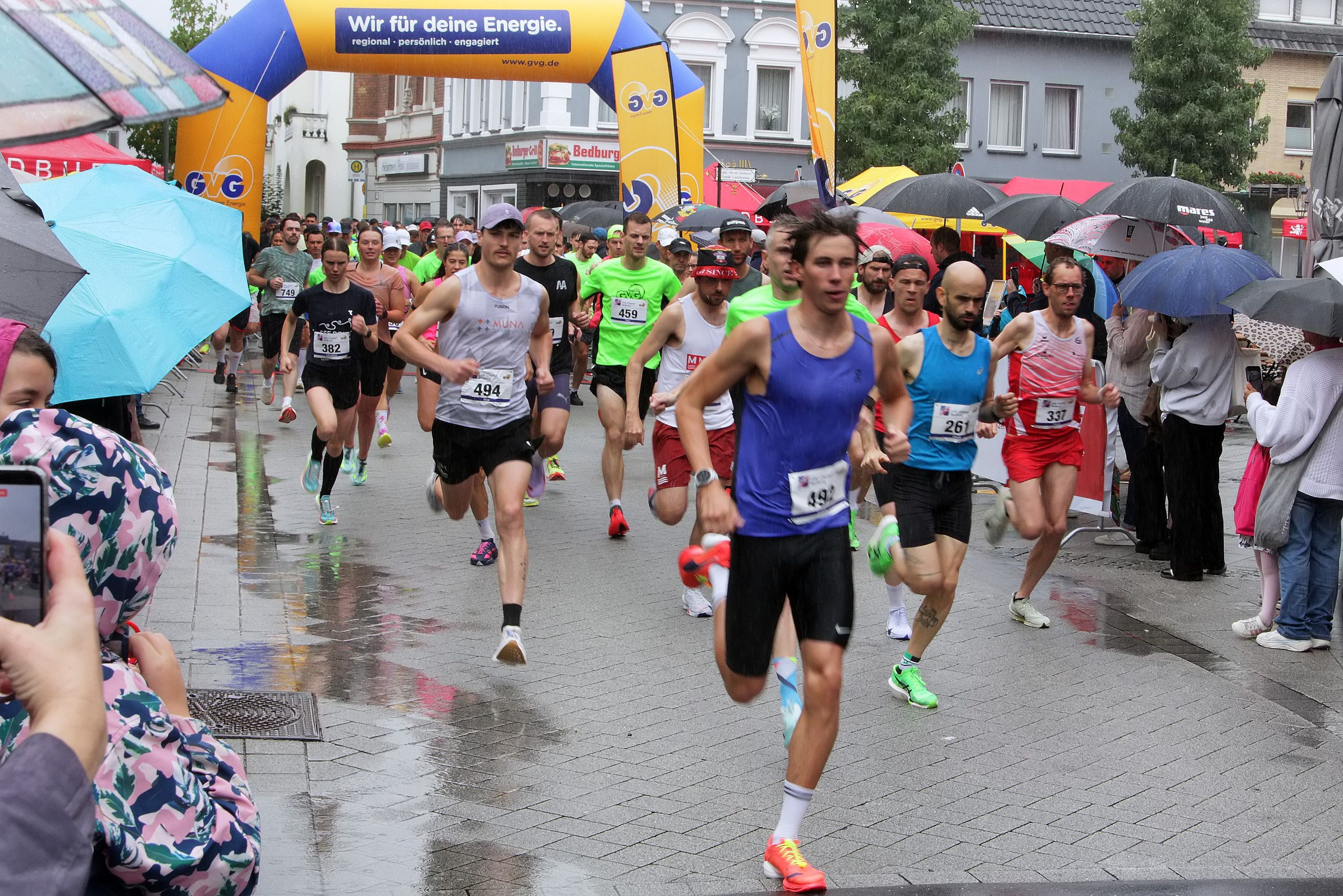 Auf dem Bild sind Teilnehmer und Zuschauer eines Laufs im Regen zu sehen.