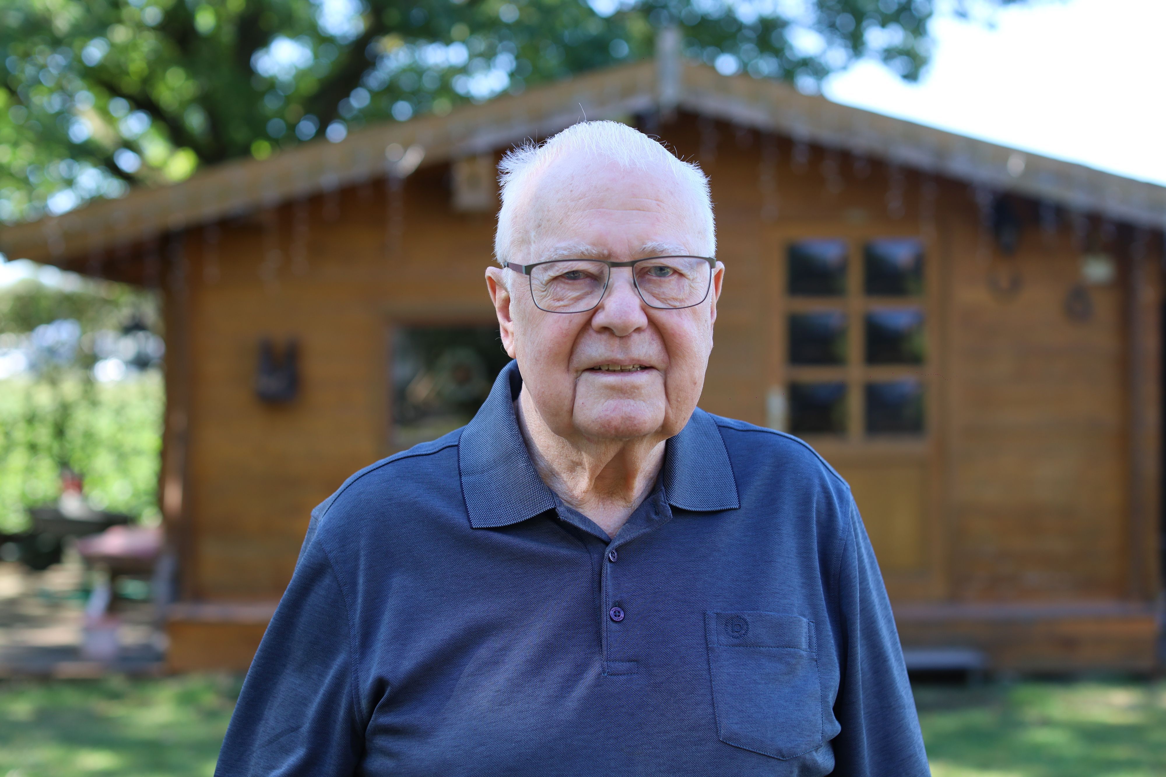Roland Kierspel ist 88 Jahre alt. Er ist im Garten vor einem Schrebergartenhaus aus Holz zu sehen.