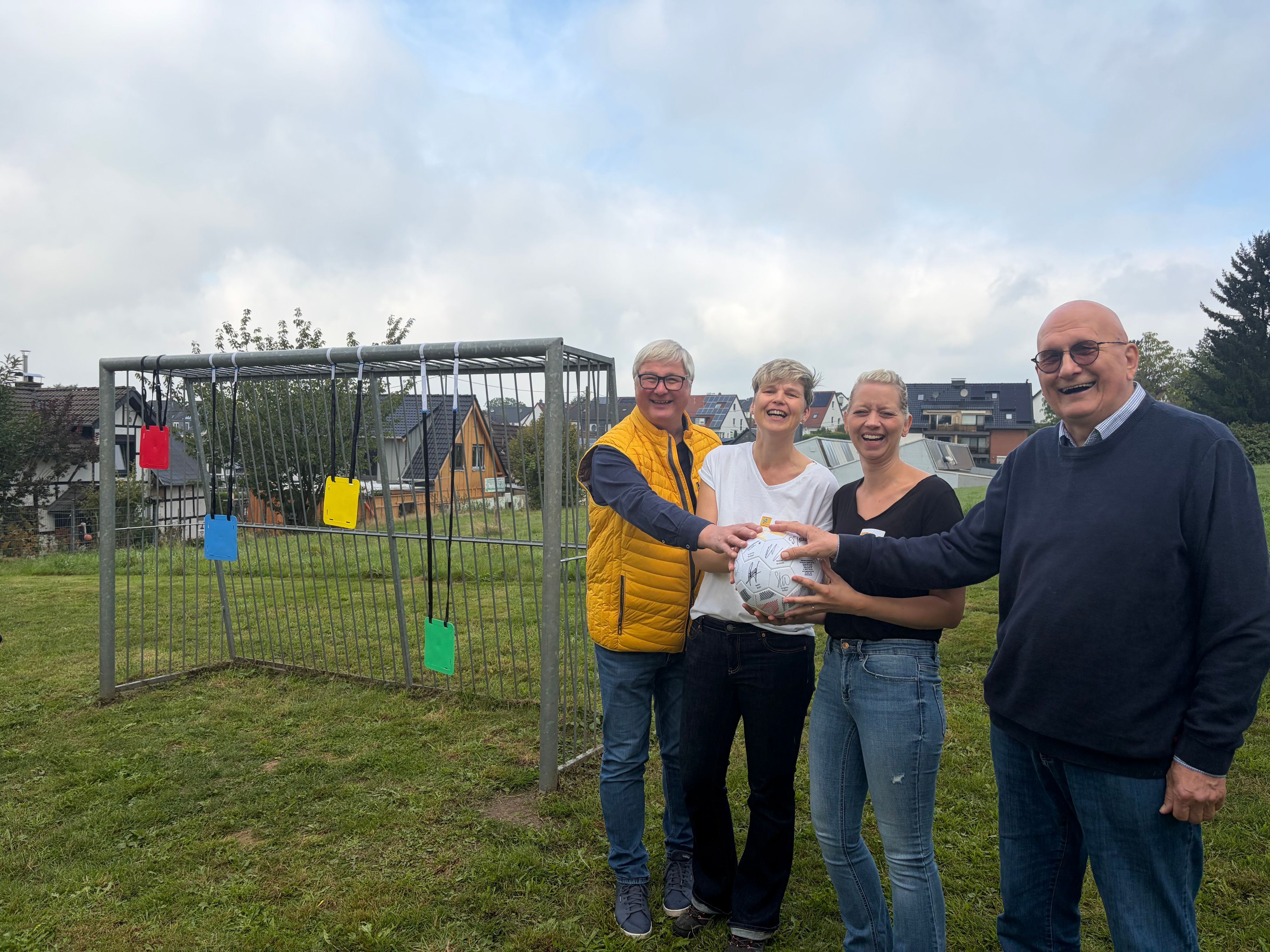 Zwei Männer und zwei Frauen stehen auf einem Bolzplatz.