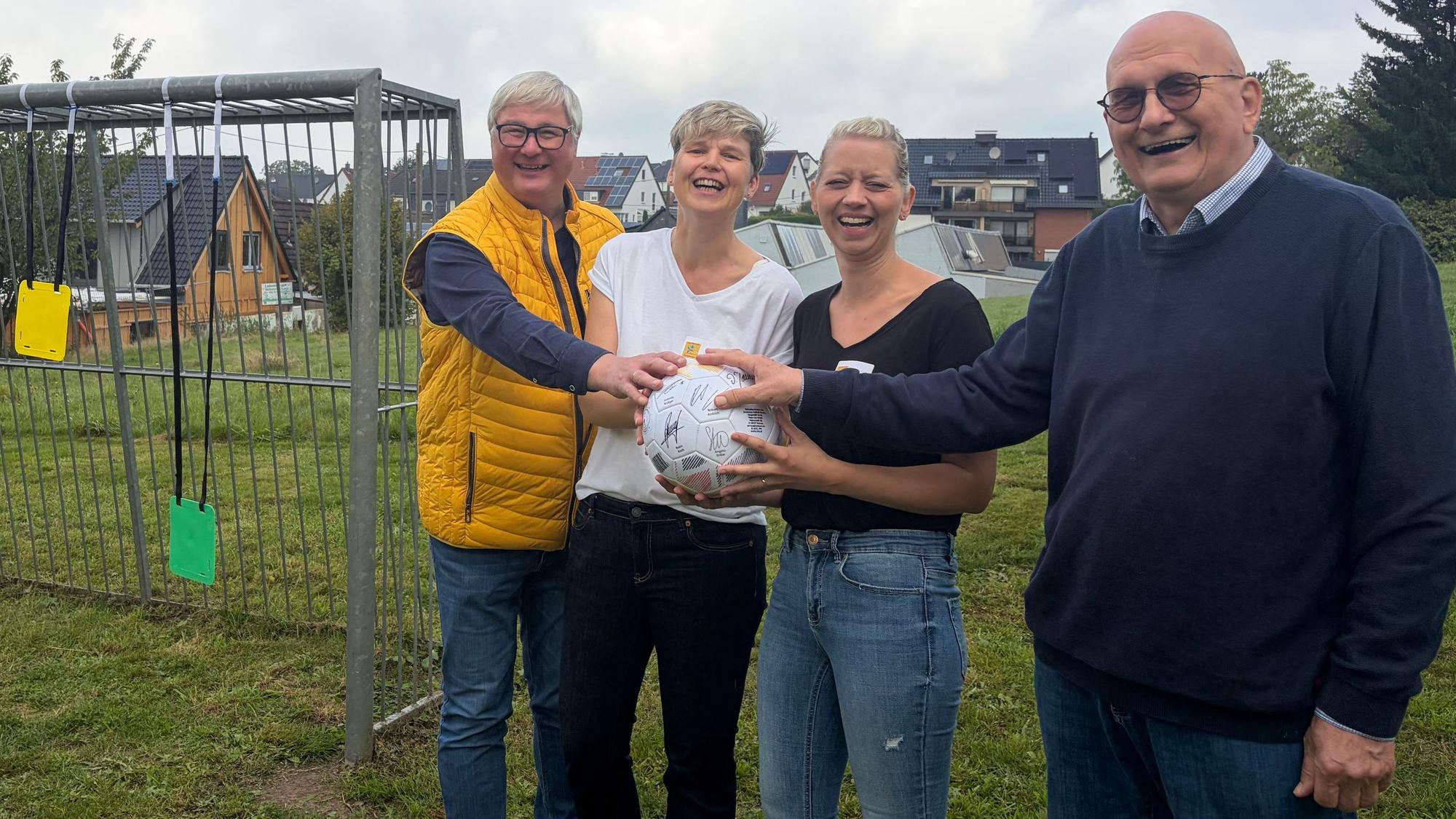 Zwei Männer und zwei Frauen stehen auf einem Bolzplatz.