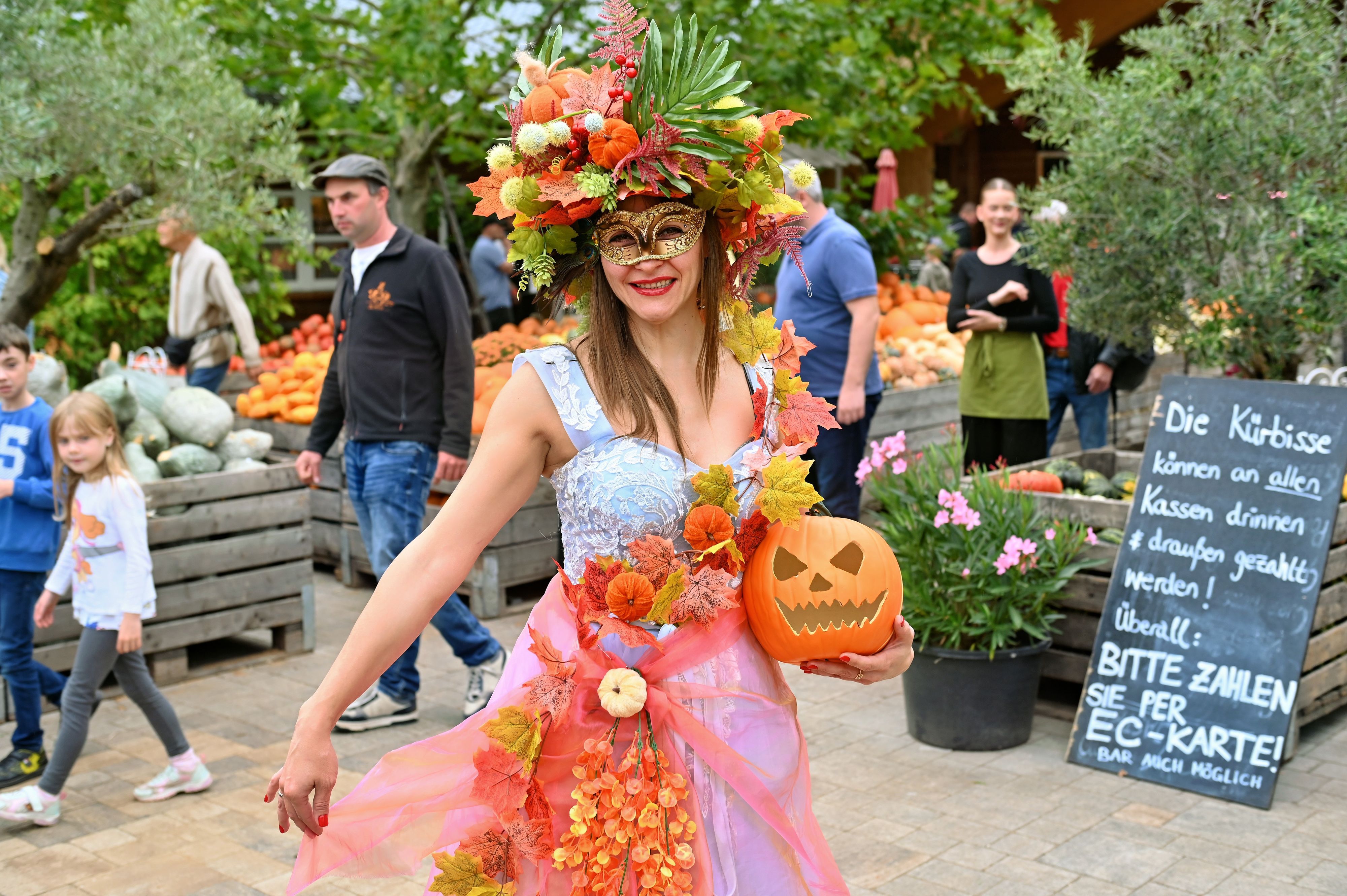 Kürbiskönigin Nataliia trägt einen Halloween-Kürbis in der Hand und ein Kleid sowie Kopfschmuck mit Herbstlaub und kleinen Kürbissen.