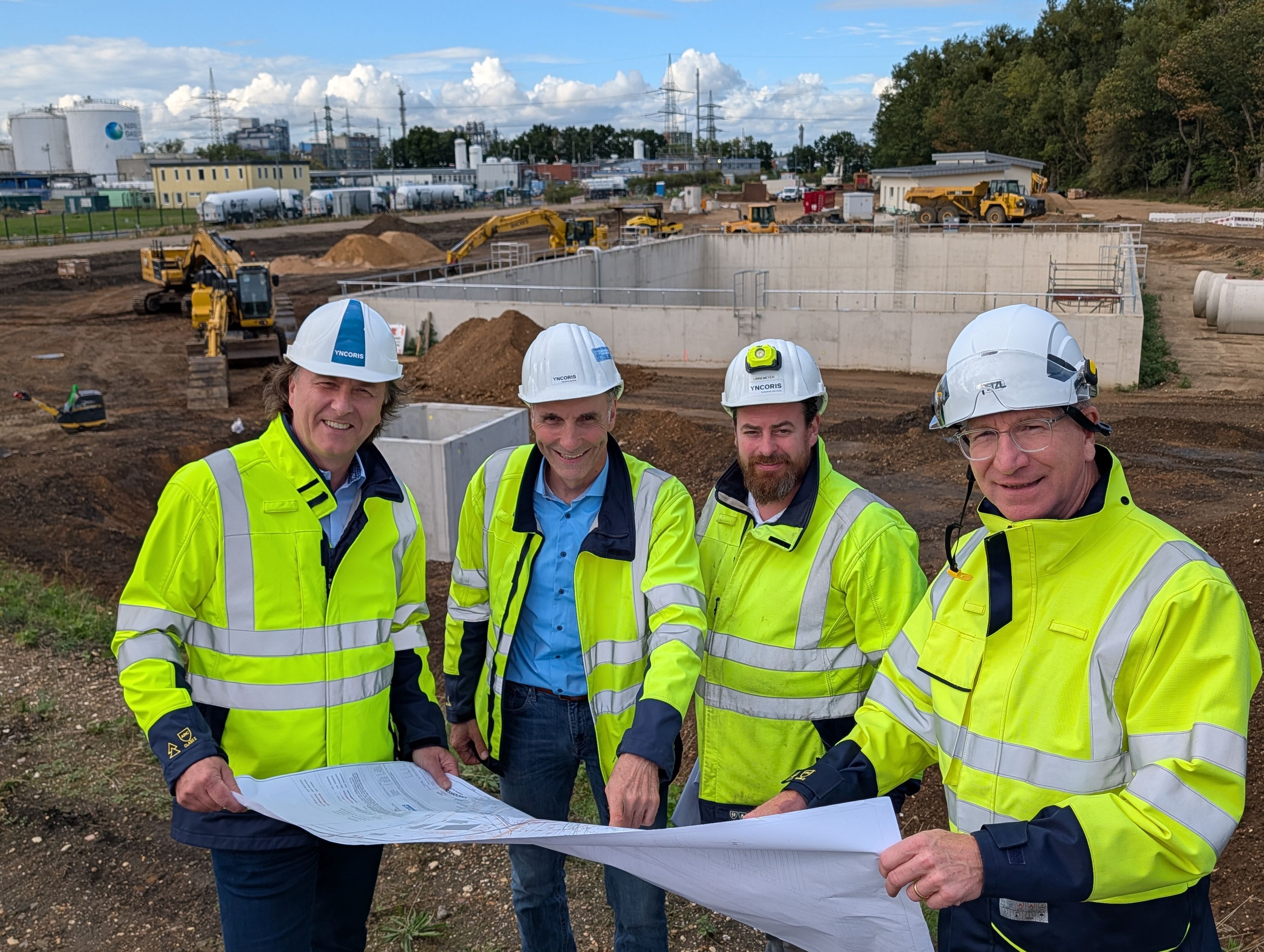 Das Foto zeigt vier Männer mit Helmen und Sicherheitswesten auf der Baustelle.
