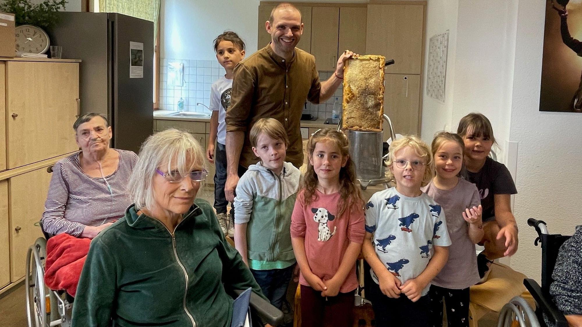 Fünf Kinder der Kita „Alexianer Pänz“ stehen mit zwei Hospiz-Bewohnerinnen, die im Rollstuhl sitzen, in der Küche des Alexianer-Hospiz in Köln-Rondorf
