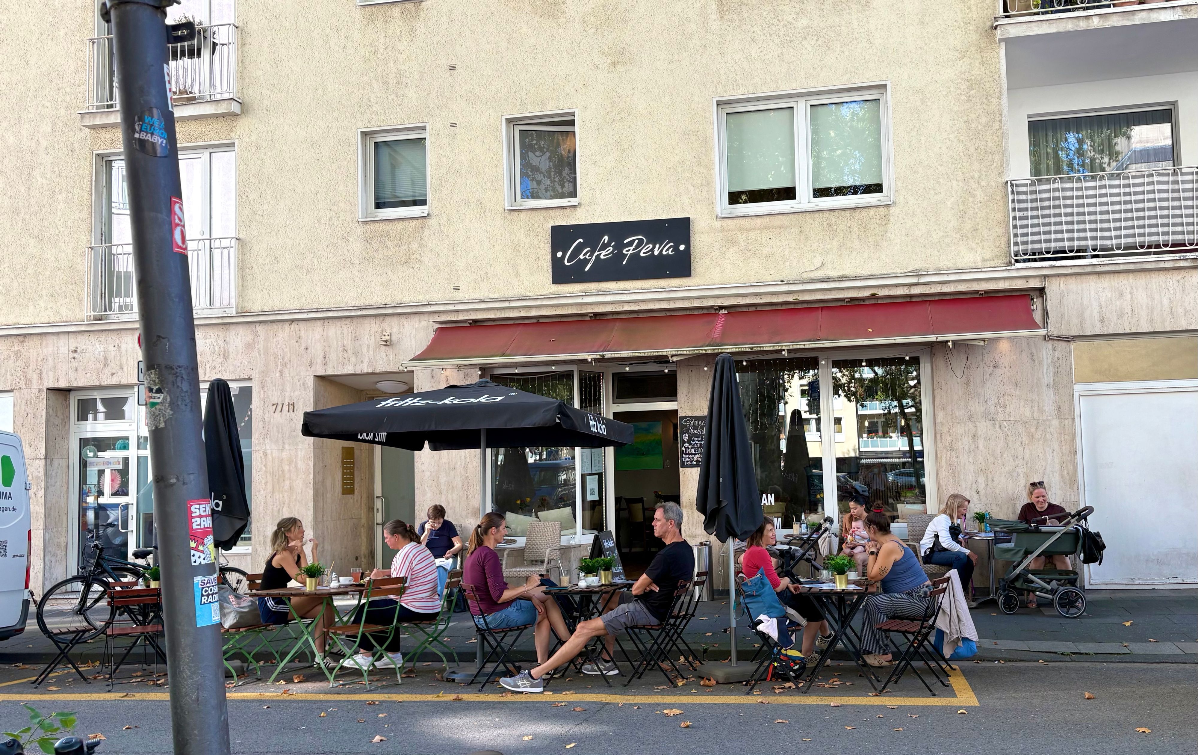 Das Café Peva in der Südstadt in Köln von außen, vor der Tür sind Sitzplätze und Tische, auf denen Gäste sitzen.