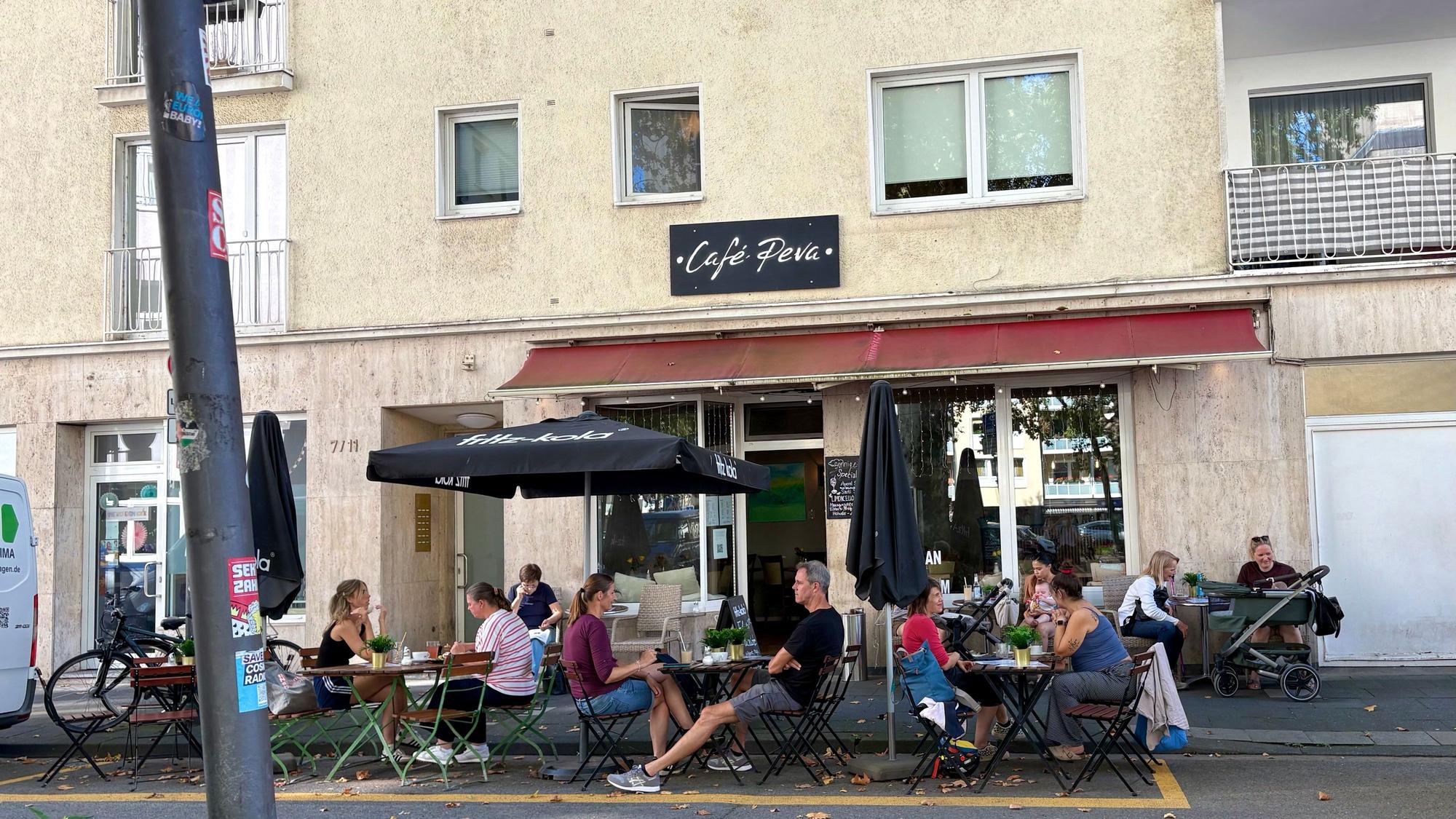 Das Café Peva in der Südstadt in Köln von außen, vor der Tür sind Sitzplätze und Tische, auf denen Gäste sitzen.