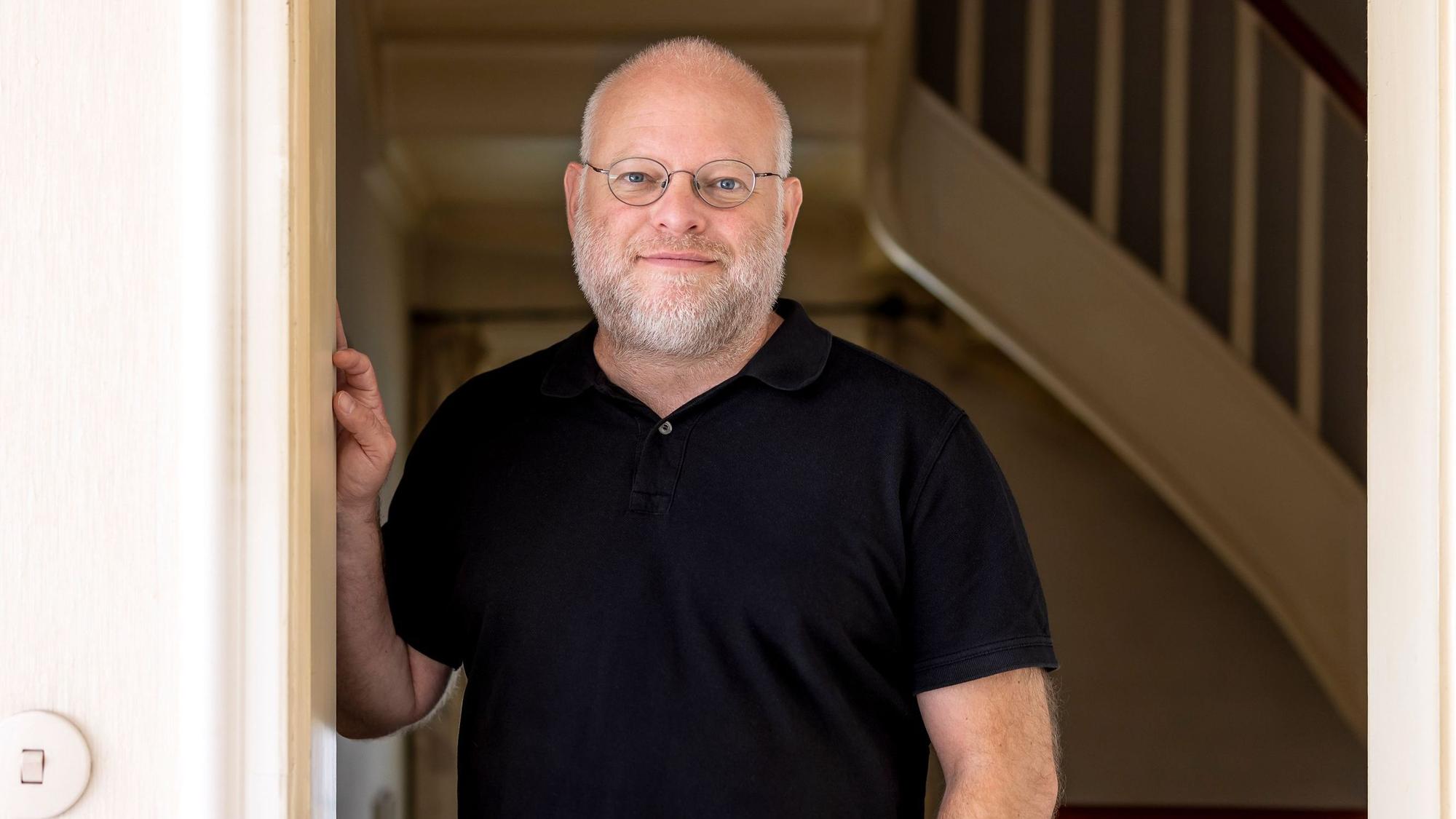 Kristof Magnusson steht an einen Türrahmen gelehnt. Er trägt ein schwarzes Polohemd.