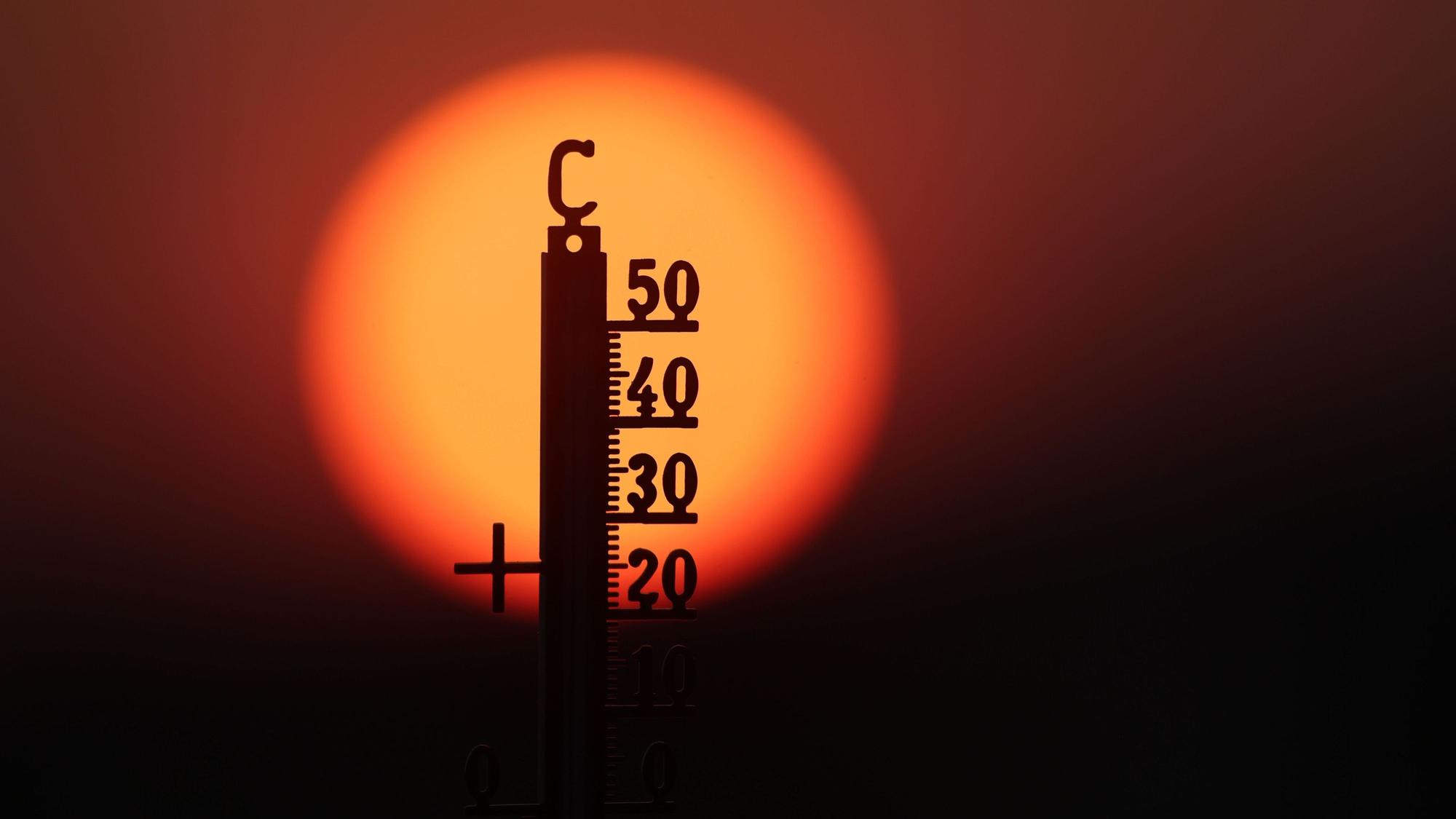 Hinter einem Thermometer geht am Morgen die Sonne auf.