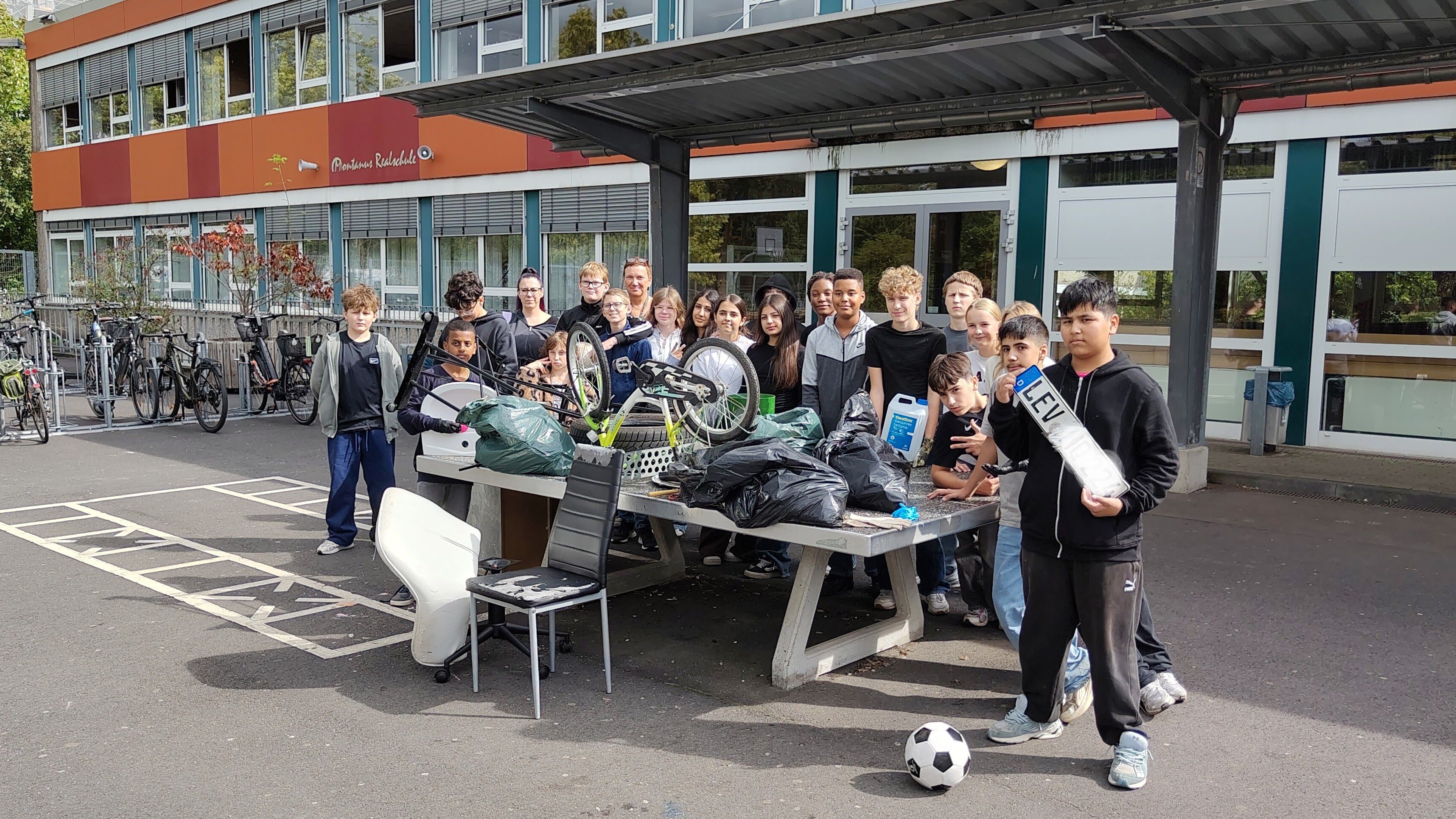 Eine Klasse zeigt ganz unterschiedlichen Müll, der gesammelt wurde: von einem Kennzeichen über Fußbälle bis hin zu einem kleinen Fahrrad.