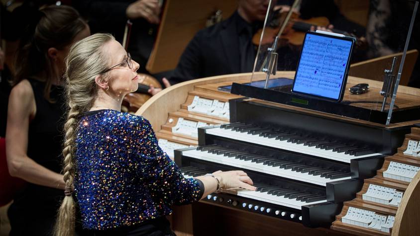 Eine Frau im glitzernden Oberteil sitzt an der Orgel.