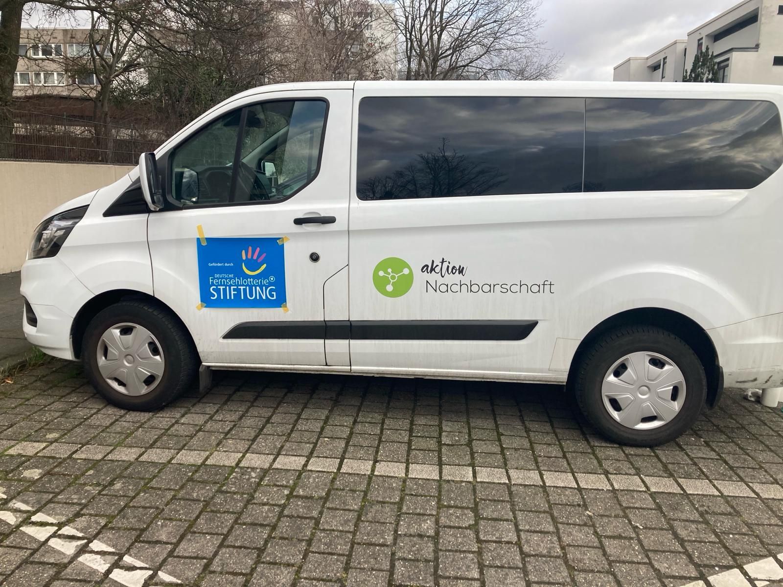Ein weißer Transporter mit der Aufschrift „Aktion Nachbarschaft“ steht auf einem Parkplatz.