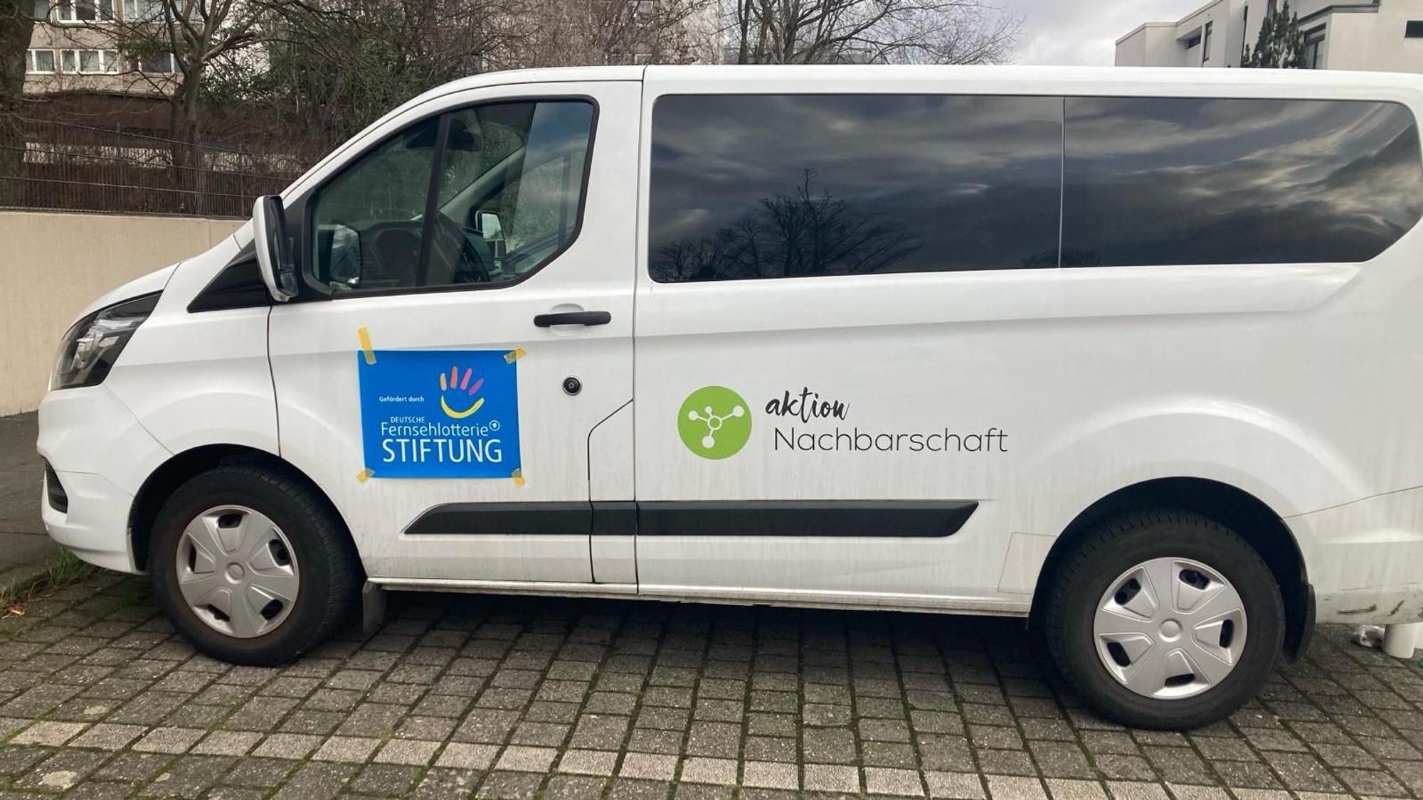 Ein weißer Transporter mit der Aufschrift „Aktion Nachbarschaft“ steht auf einem Parkplatz.