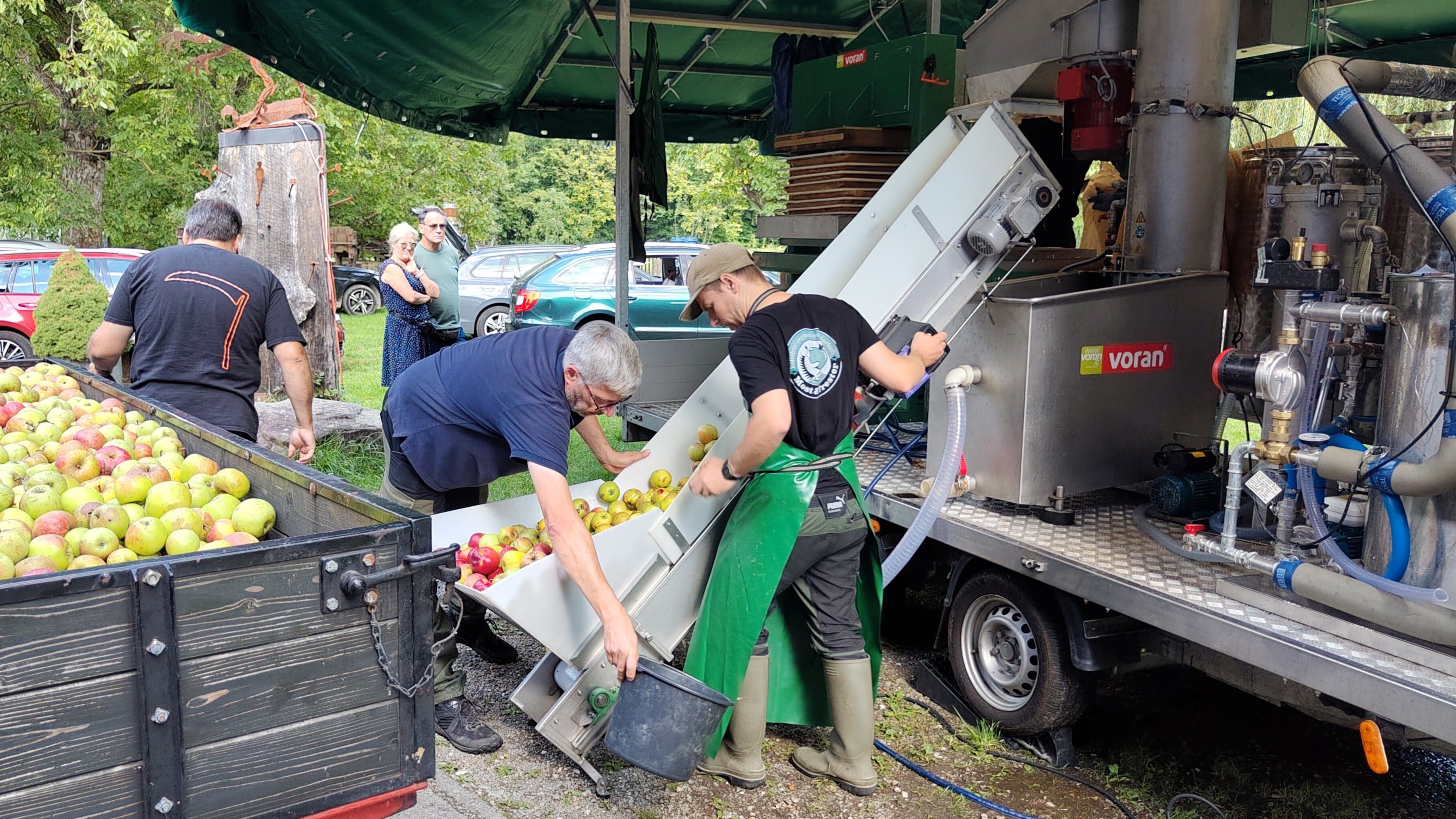 Äpfel werden von zwei Männern für die Maschine nachgefüllt.
