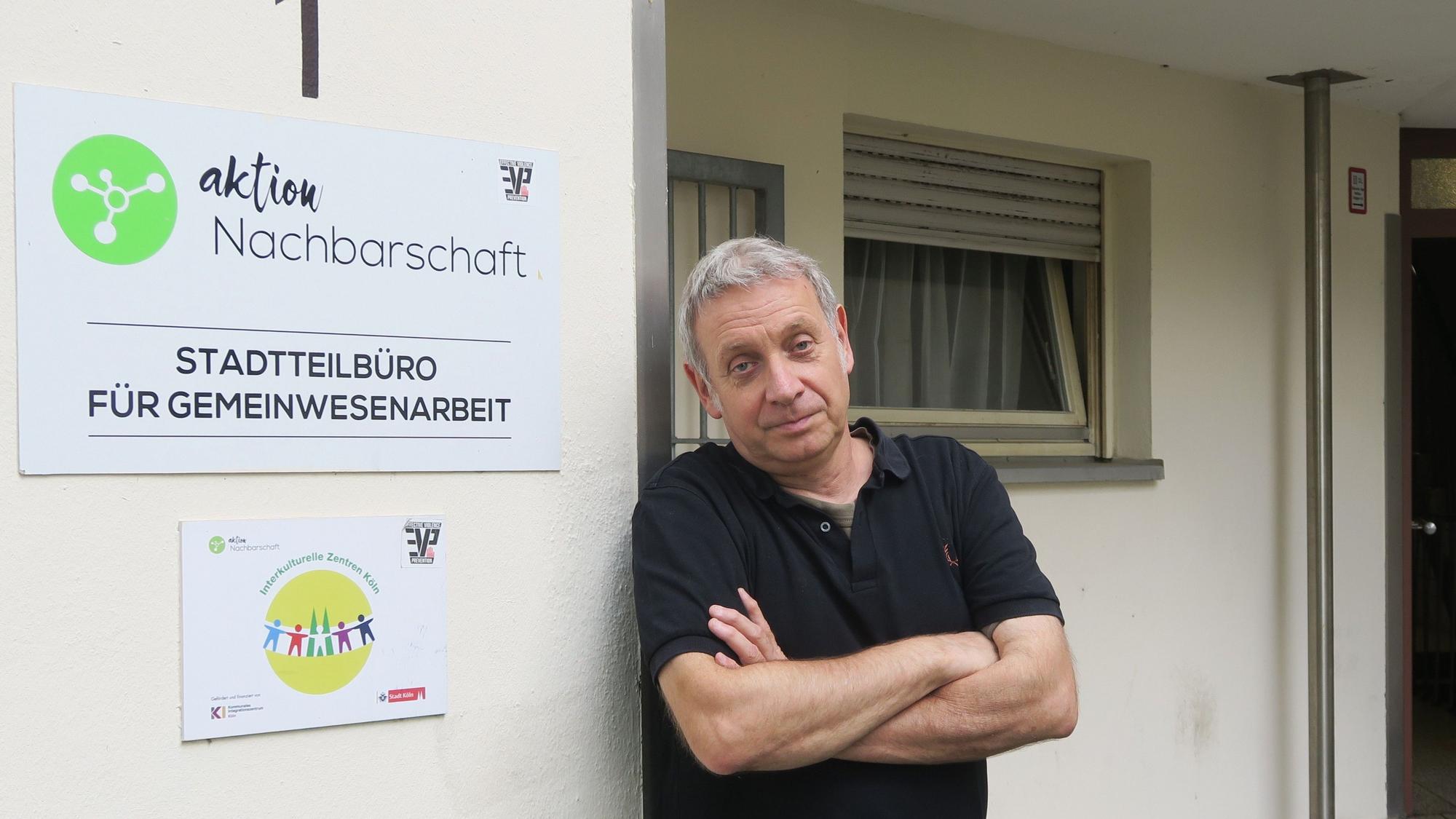 Ein Mann im schwarzen Poloshirt lehnt an einer Hauswand.