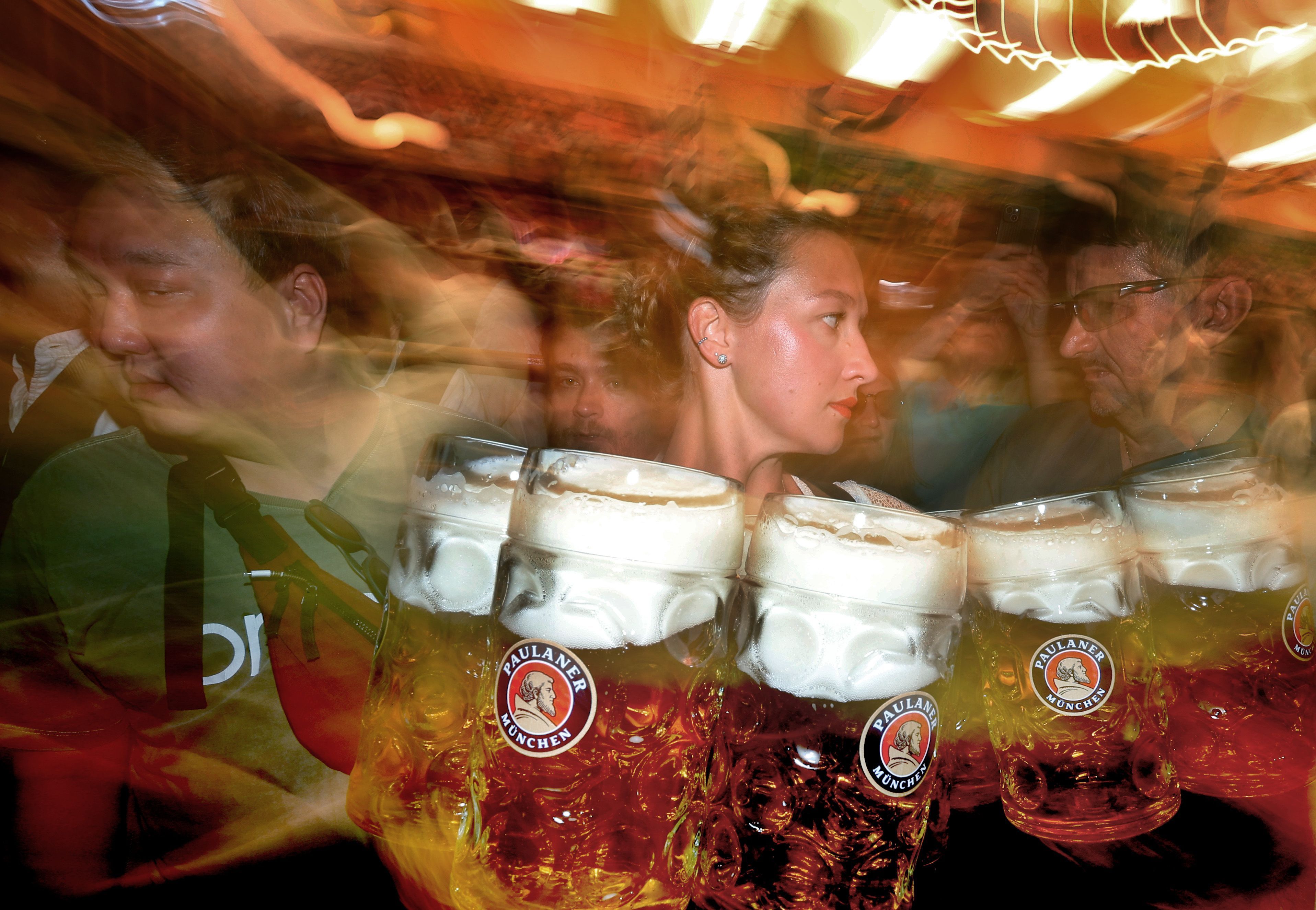Eine Bedienung trägt im Paulaner-Festzelt Maßkrüge mit Bier (Unschärfe durch lange Belichtungszeit).